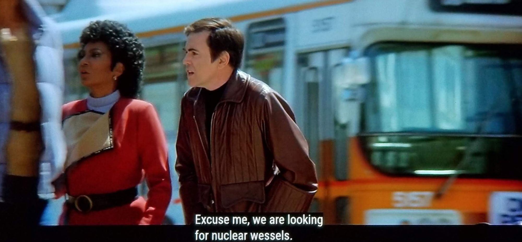 Scene from Star Trek IV: The One with the Whales. Chekhov and Uhura are on a busy street with a city bus circa 1980s in the background. Uhura is in her red uniform but with the dinner flap open for casual time. Chekhov is in a sweet but dated leather jacket. It looks like a nice day, maybe high 60s or low 70s. Closed caption reads, "Excuse me, we are looking for nuclear wessles."