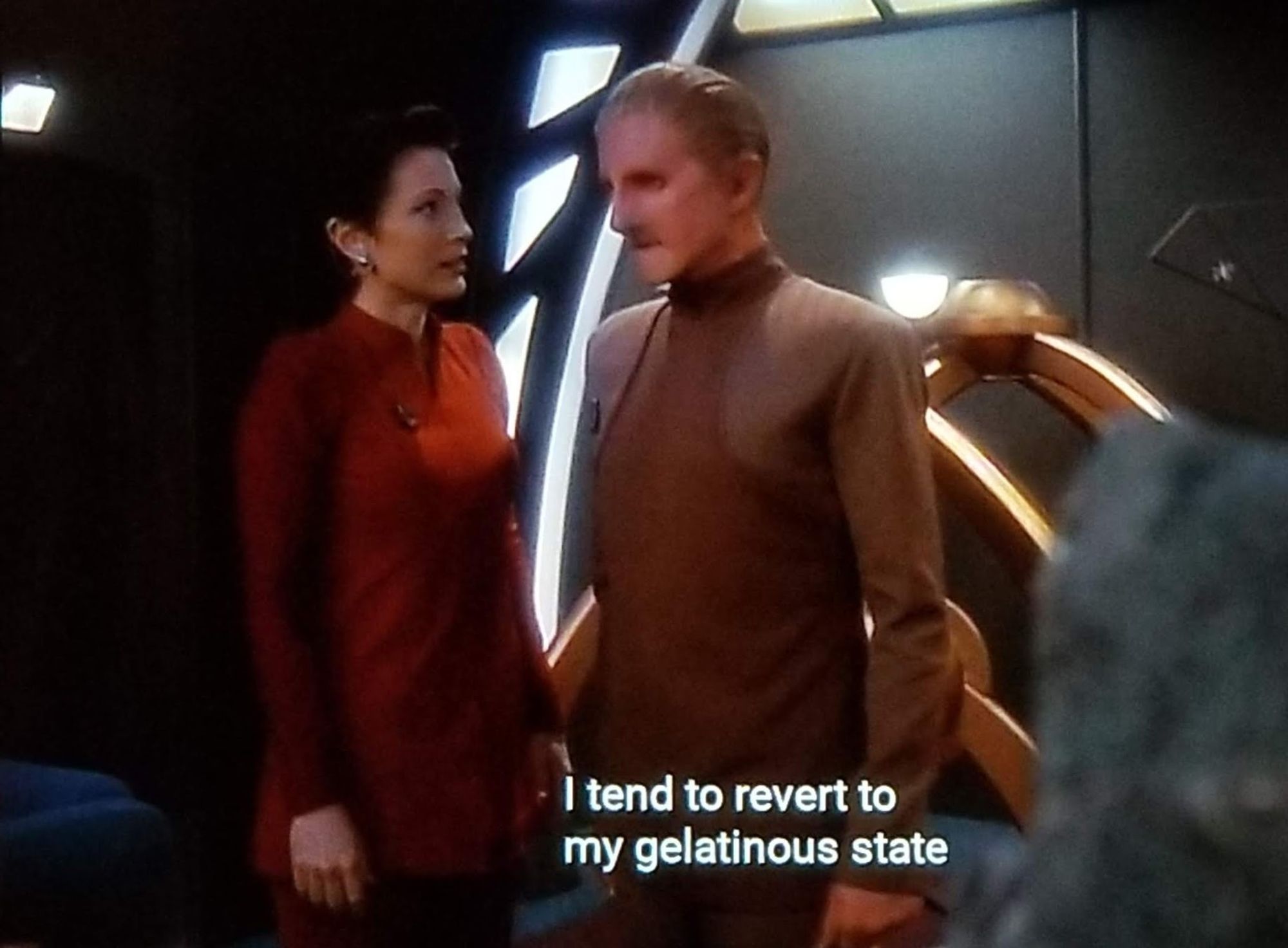 DS9 scene. Odo and Kira are standing and talking. Kira is in her red/maroon uniform and is wearing some ear bling. Odo is wearing his classic tan on tan on brown on tan look. Closed caption reads, "I tend to revert to my gelatinous state and slide onto the floor."