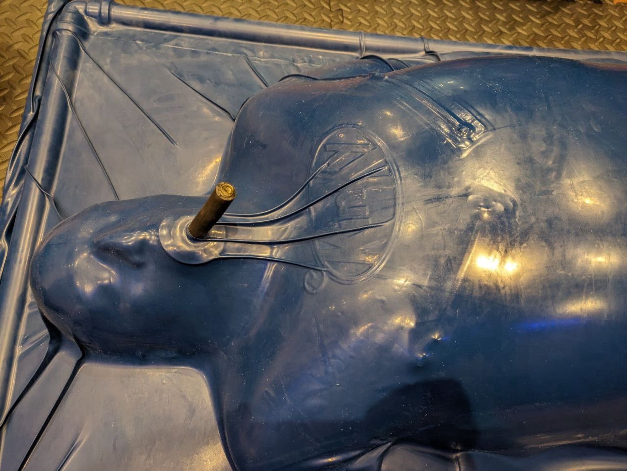 Close up of head and chest in a blue vac rack.

The KinKy logo and nipple zips clearly visible through the taught airless rubber vac bed with the occupant just able to breath through a small tube gag