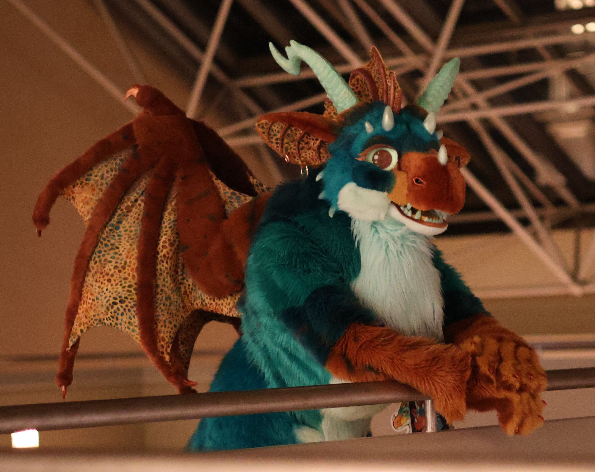 Avala the dragon fursuit leaning on a railing.