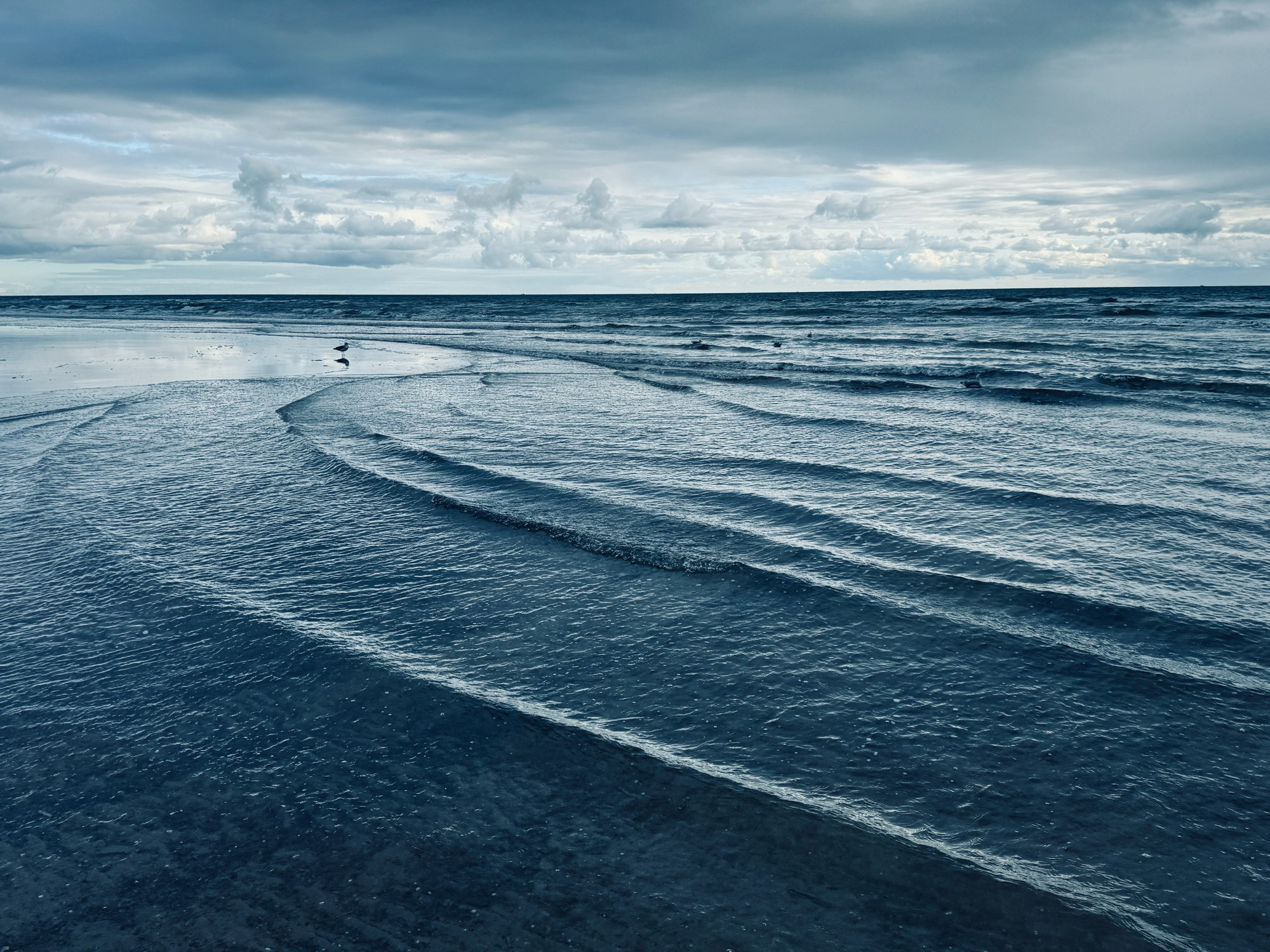 Blick aufs Meer. Man sieht sanfte Wellen und den Wolken bedeckten grau-weiß verhangenen Himmel. Das Bild ist mit einem Filter belegt, der die Blaugrautöne heraus hebt.