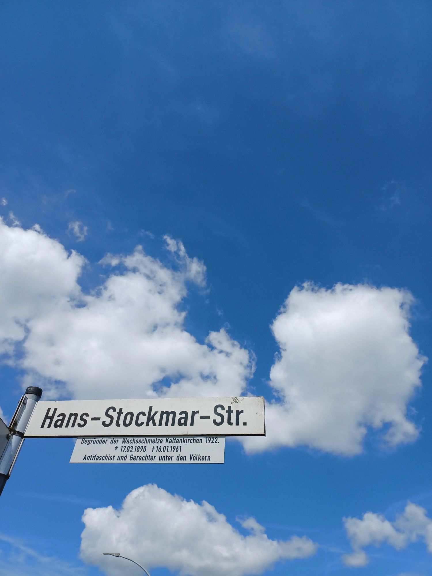 Straßenschild "Hans-Stockmar-Str." vor blauem Himmel mit weißen Wolken