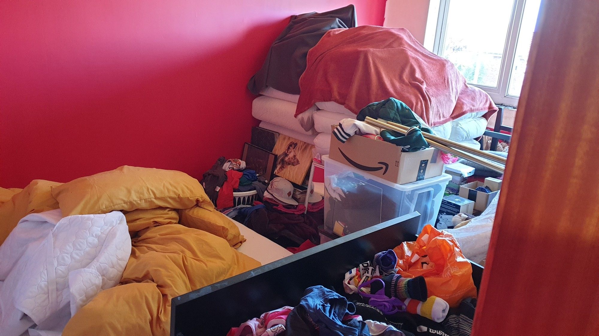 The Red Room is stacked full of stuff, in the foreground a mattress sits on the floor, linen just piled uncermoniously on top