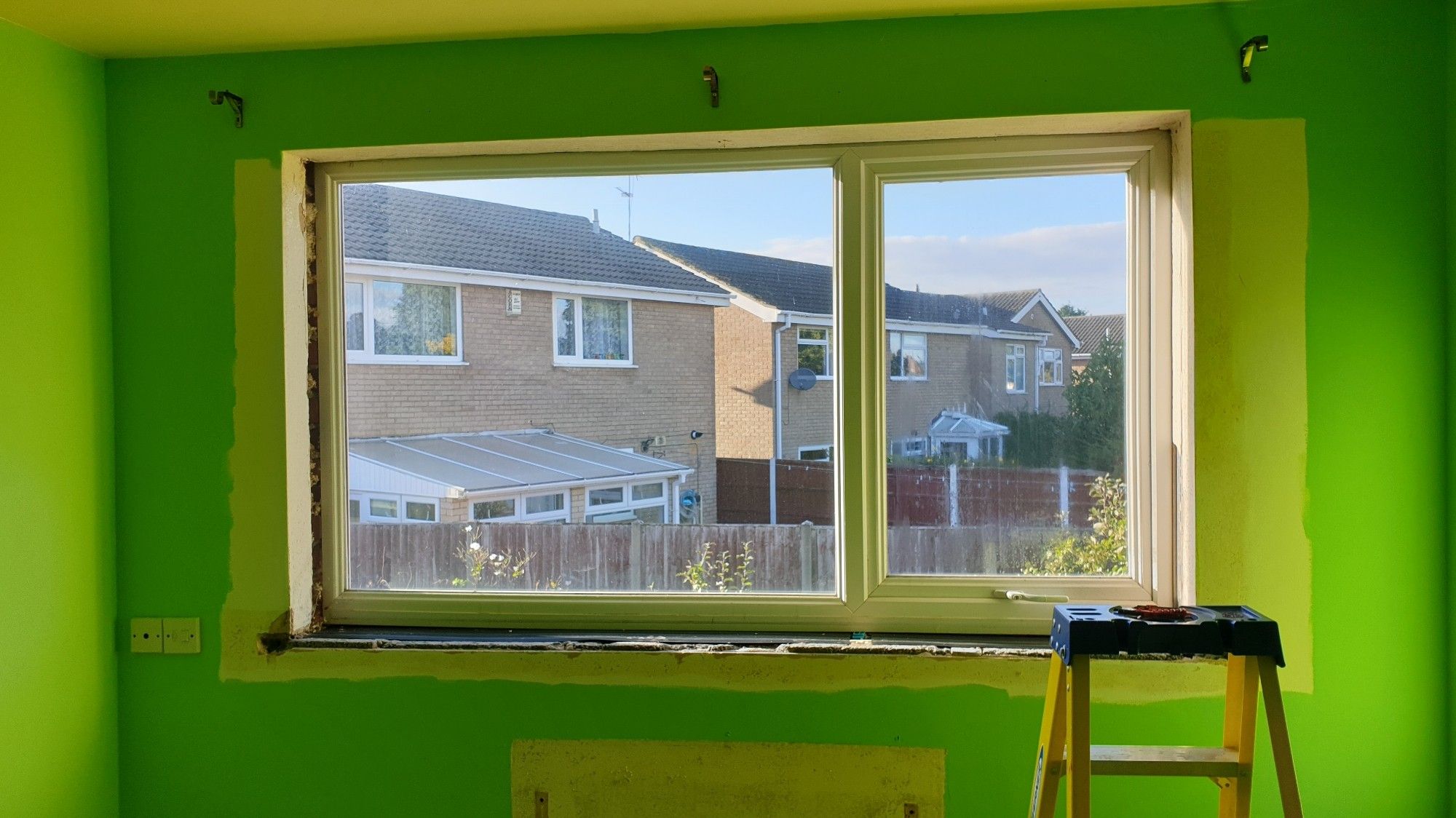 The Green Room. The photo is focused on one wall which has a window in it. The whole window surround is unpainted, the sill is removed revealing bare concrete, one side has an open cavity, and the plastering where the sill was is ruined.