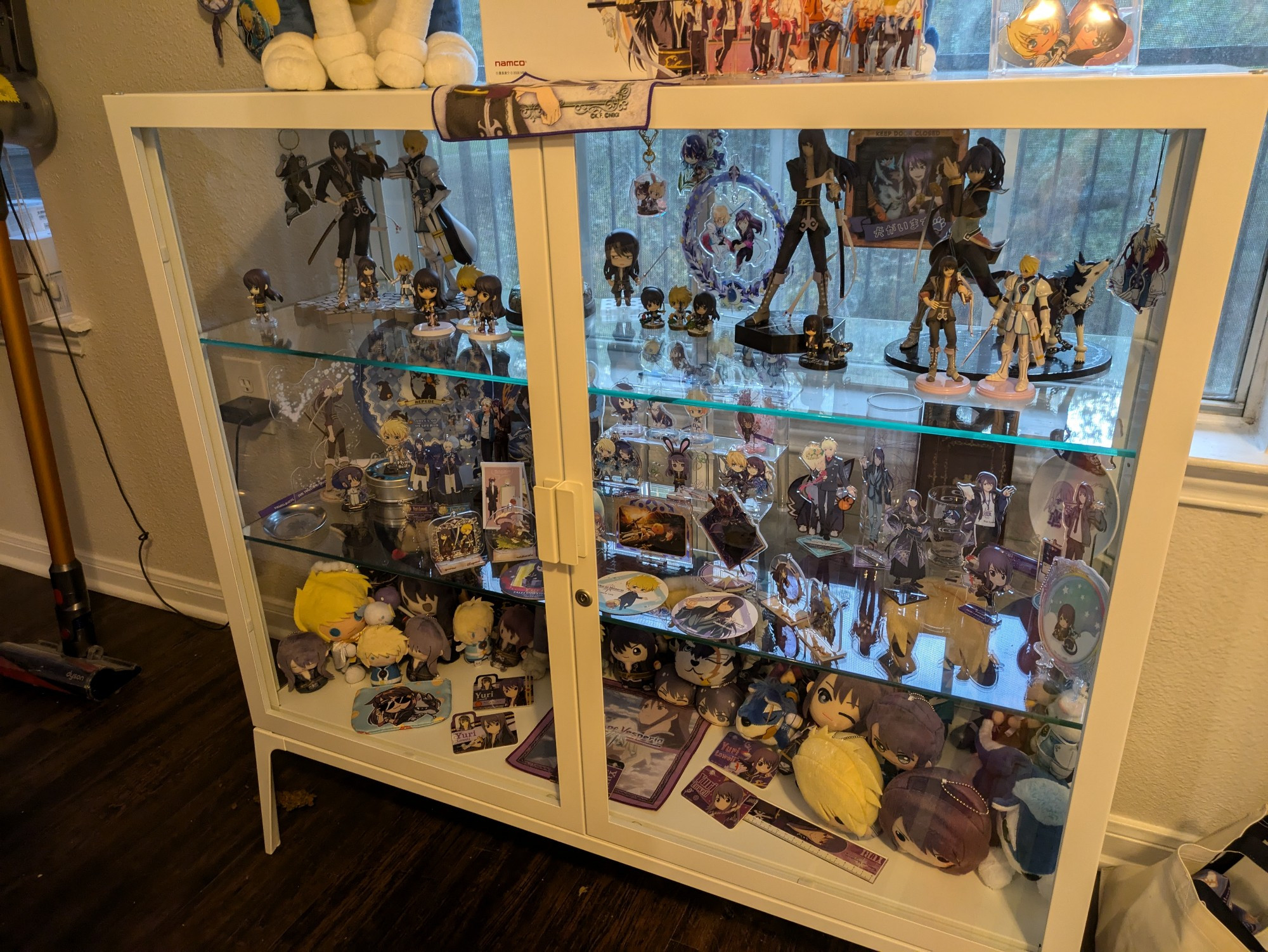 a closer view of the items inside the display shelf. these include plates and glasses, acrylic stands, figures, and plushies, among other things