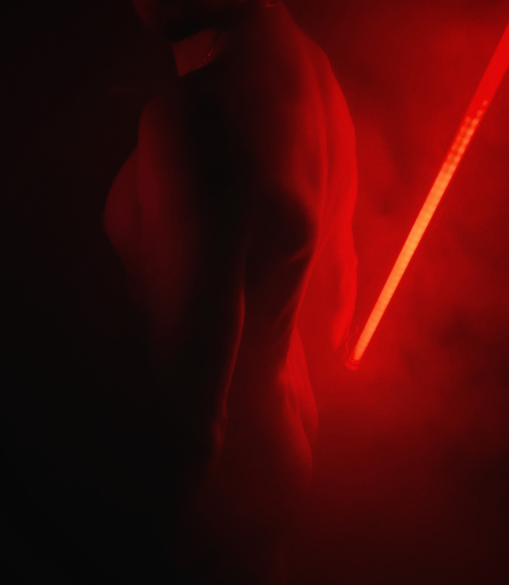 Younglandsuit wearing nothing in the fog, just a red lightsaber illuminating his back and butt