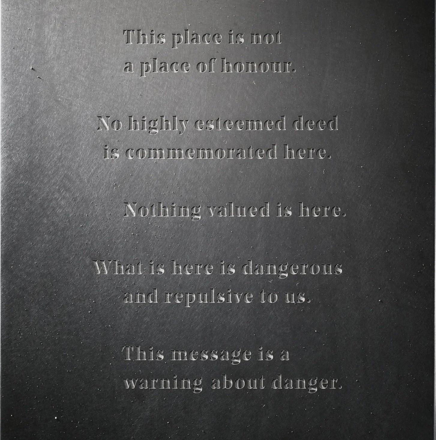 An inscription as if carved into stone, originally written as a warning to future civilizations at long-term nuclear waste storage sites.

Text reads:
This place is not a place of honor.

No highly esteemed deed is commemorated here.

Nothing valued is here.

What is here is dangerous and repulsive to us.

This message is a warning about danger.