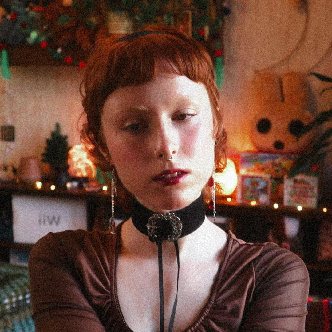 a photo of emmy in her room. she is wearing a brown top and a victorian style black choker.