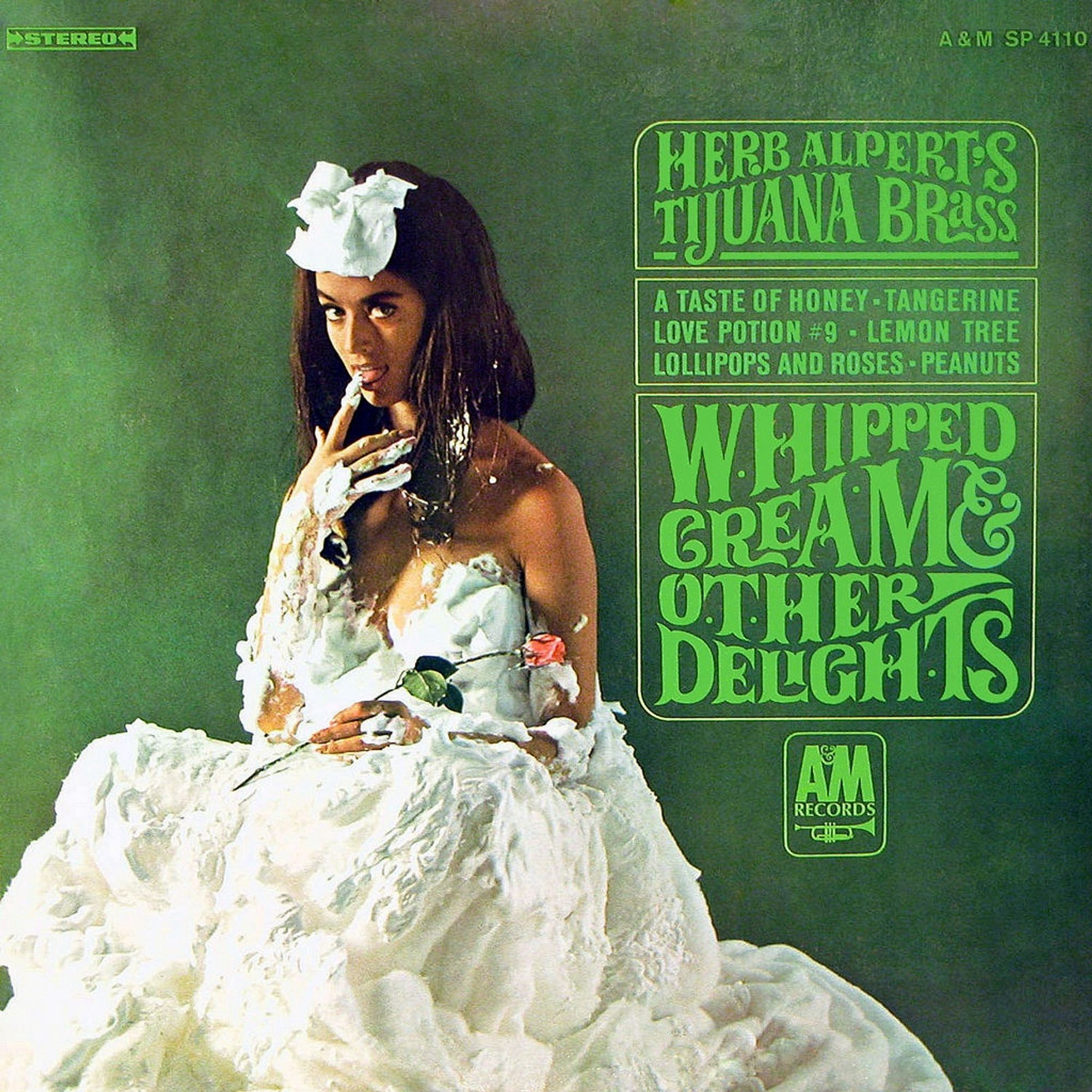 The album cover for Herb Alpert’s Whipped Cream and Other Delights. It features a seated woman covered in whipped cream, some of which she is licking off her fingers. She is holding a rose in her other hand.