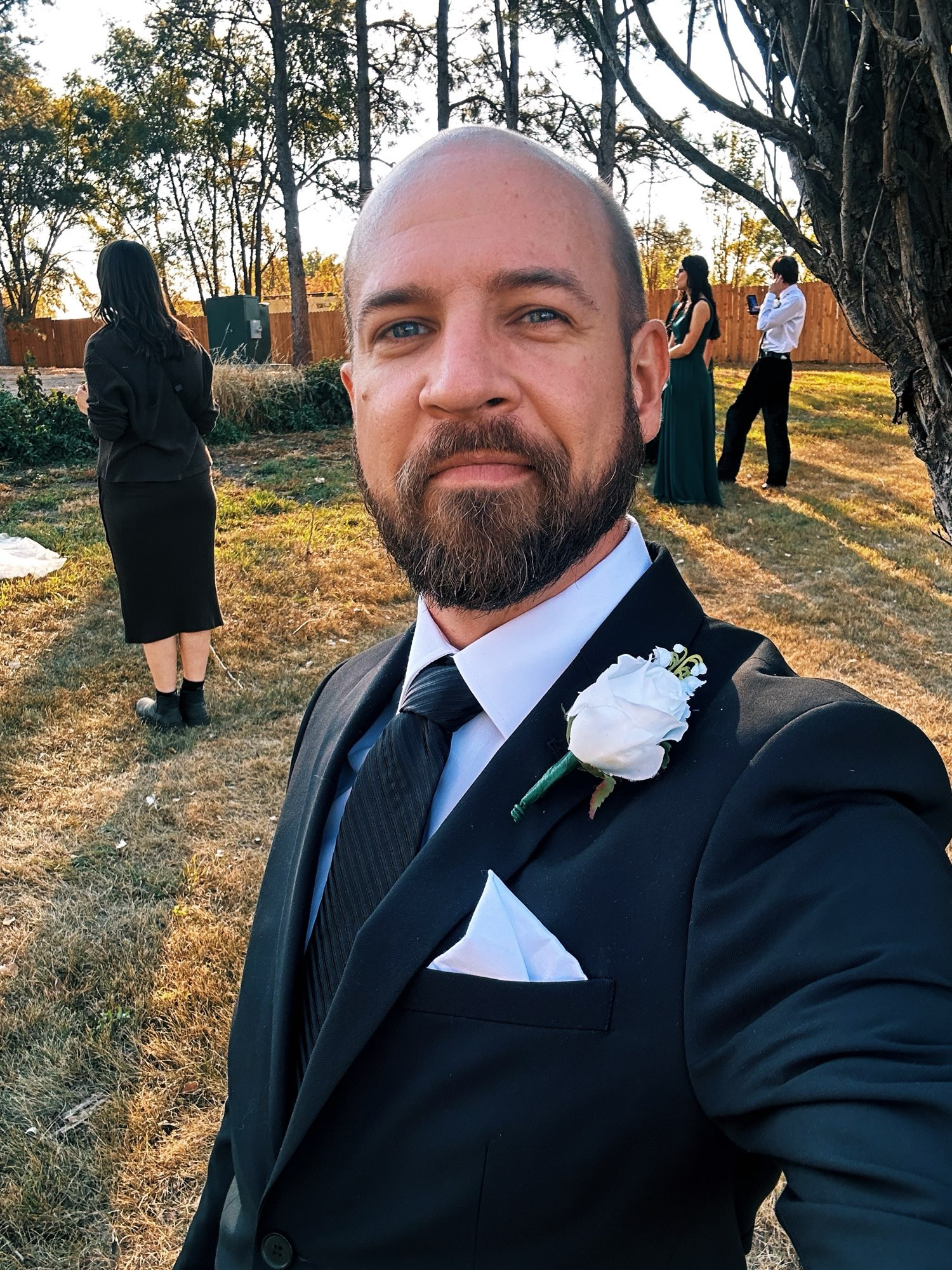 Selfie of the poster in a black suit—outside with wedding pics happening in the background.