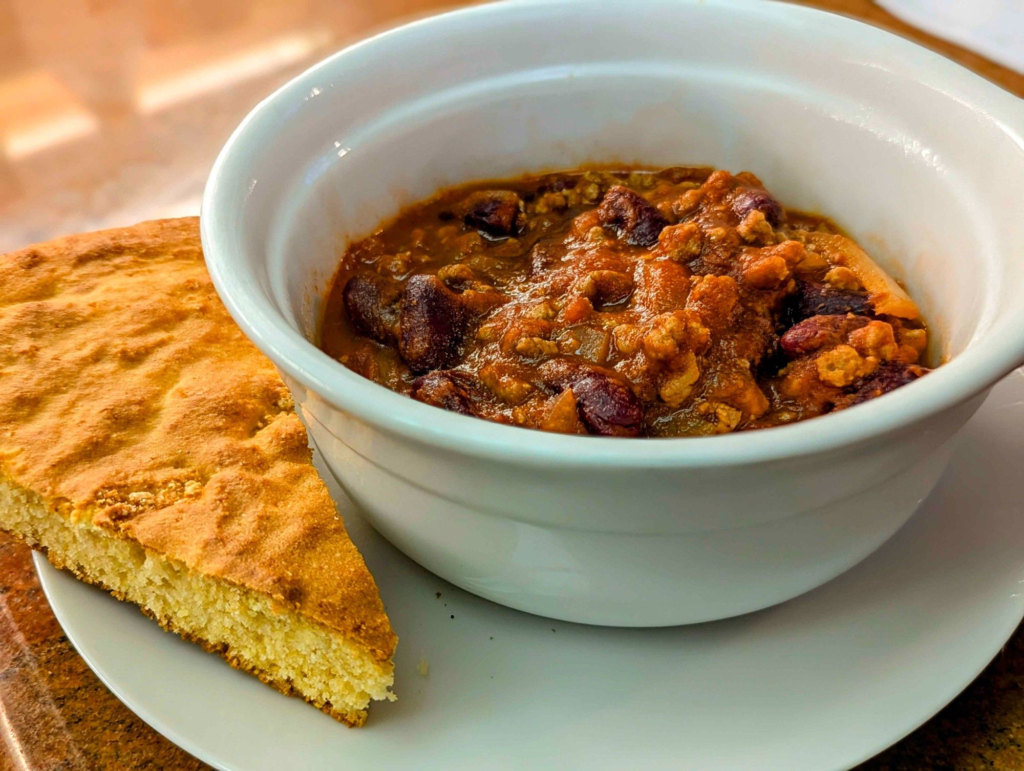 Bowl of chili with slice of cornbread to its left.