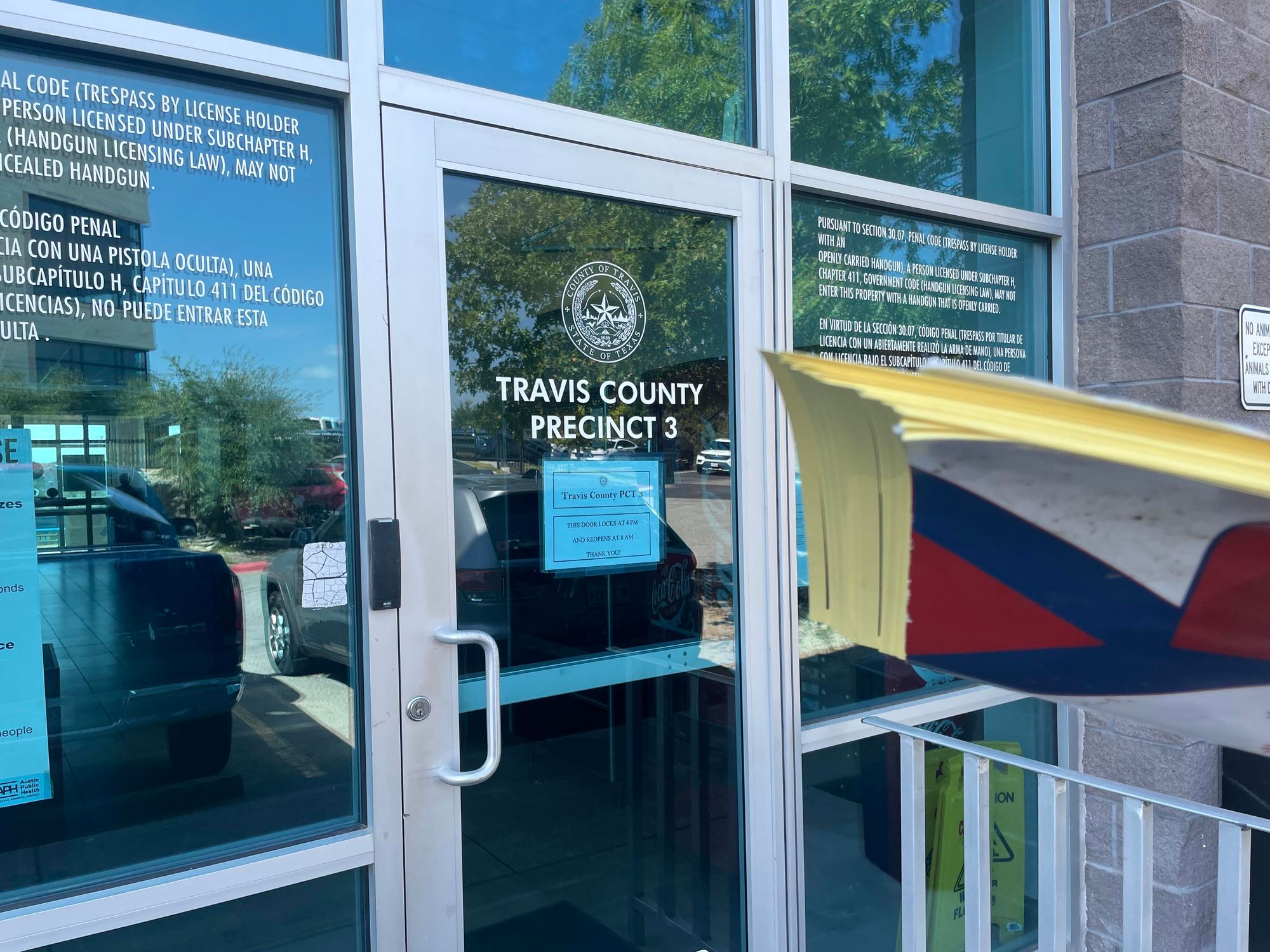 An old beat up folder overfilled with completed voter registration forms held up in front of the Travis Co Precinct 3 building doors