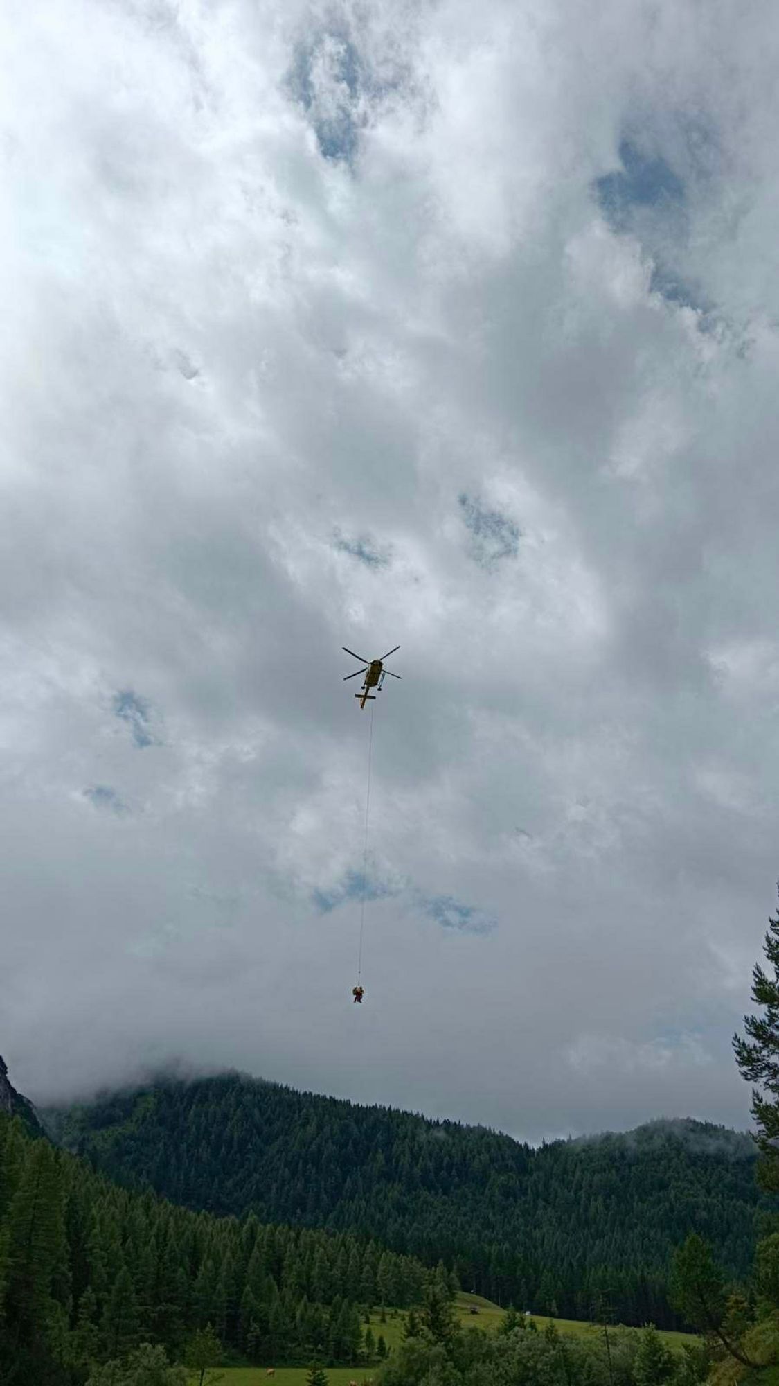 foto gegen bewölkten himmel, helikopter, daran an einem seil baumelnd zwei menschen