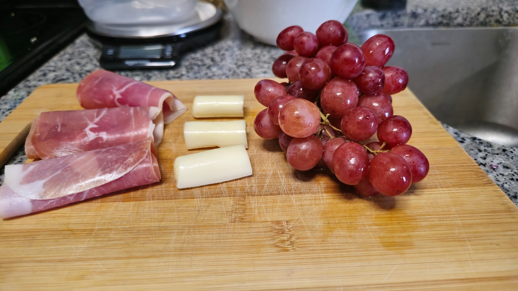 A simple charcuterie board, with 3 slices of prosciutto, string cheese (cut into 3), and a bunch of grapes.