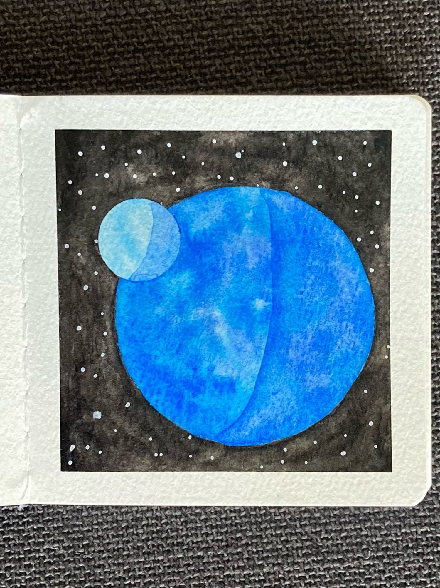 A watercolor painting of a planet and moon in space. The planet is a rich, mottled blue. The moon, half overlapping the planet to the north-west, is a pale blue. Behind them is the vastness of space, dotted with stars.