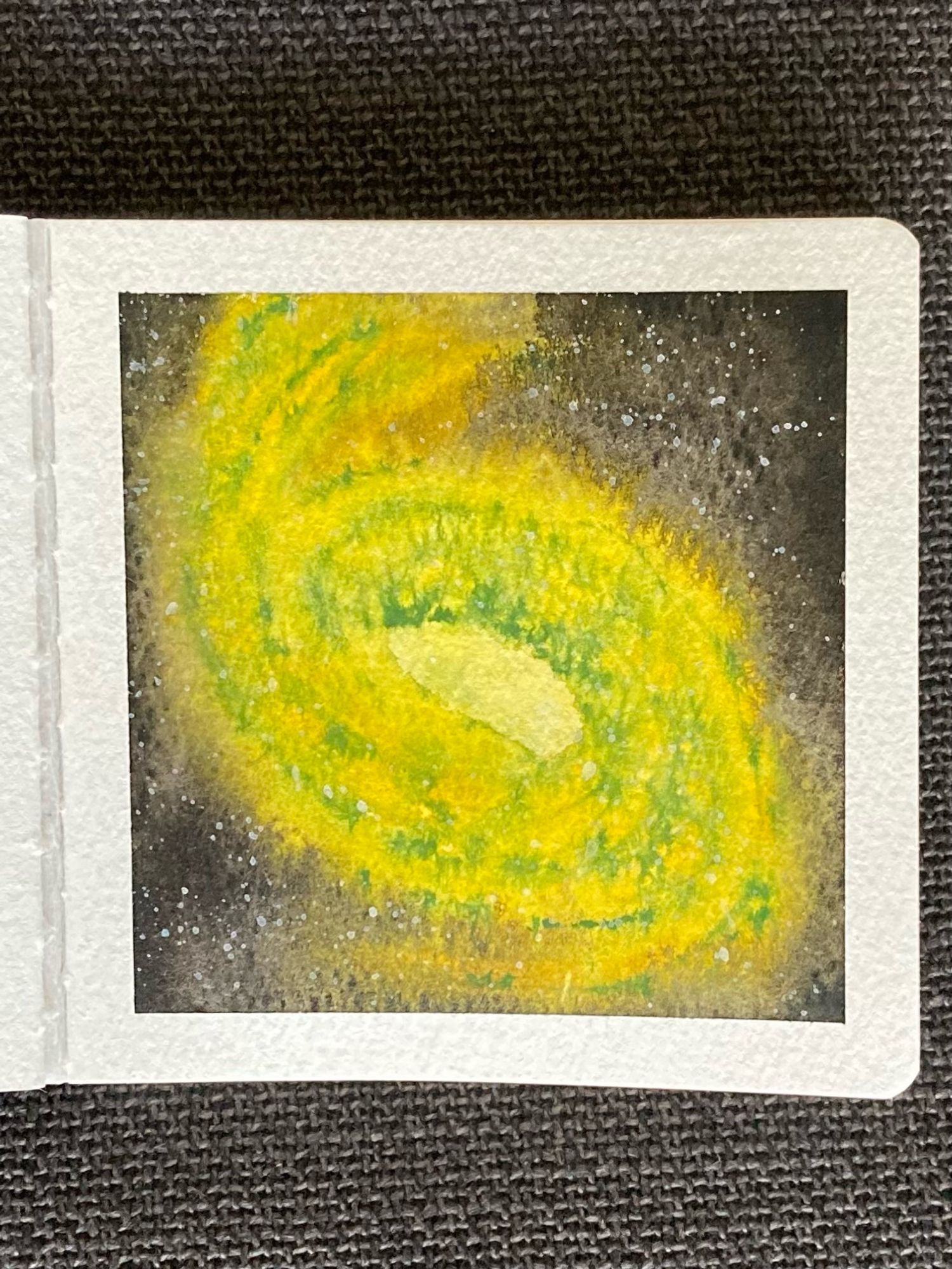 A watercolor painting of a spiral galaxy in space. It’s pictured on an angle, with yellow spiral arms reaching to the northwest and southeast. There is a central light yellow core and thin stripes of green dust clouds follow the shape of the spiral arms. Surrounding the galaxy is the vastness of space, dotted with stars.