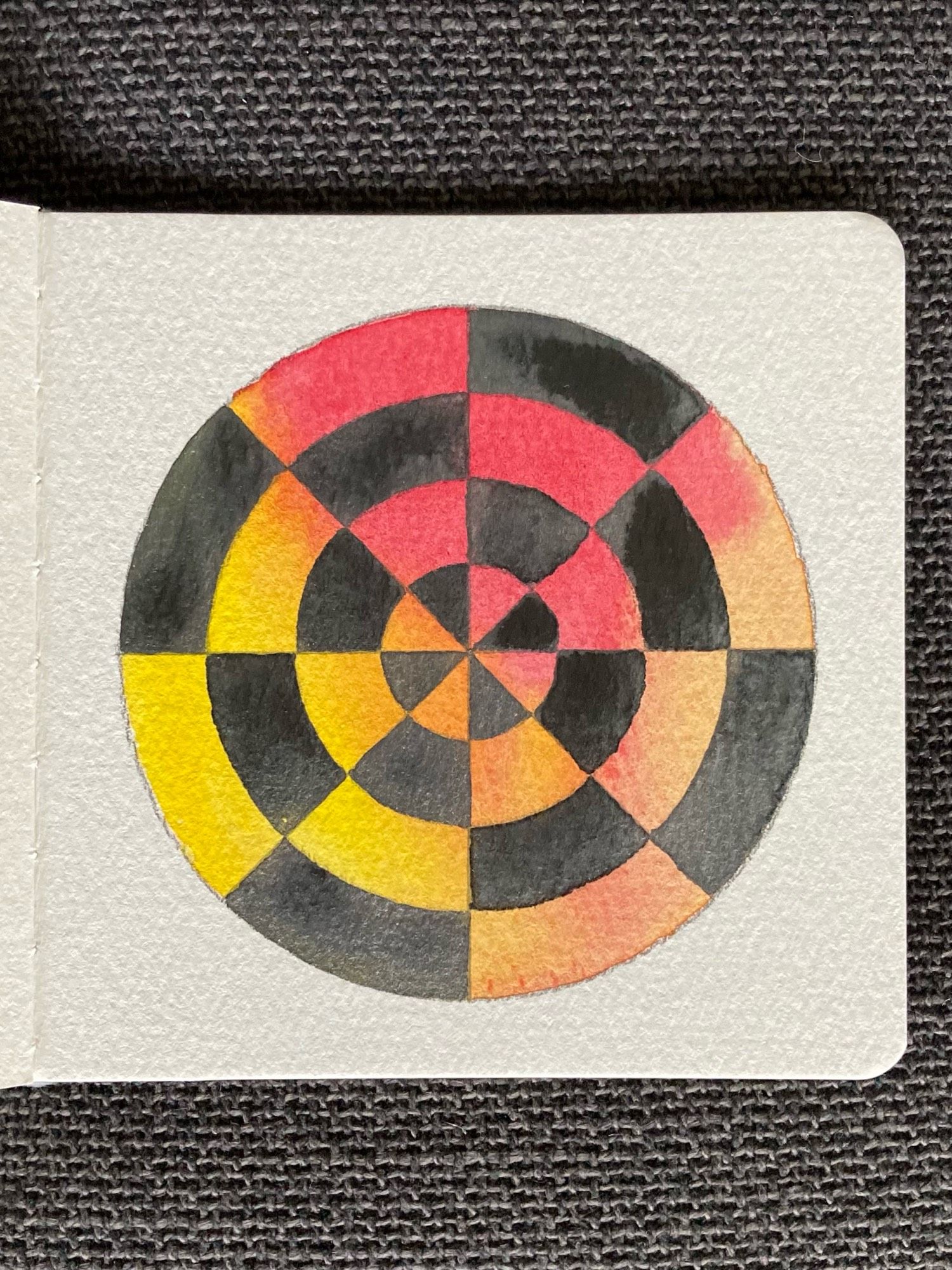 A watercolour painting of a circular grid. The background of the grid has been painted with a saturated wash of reddish pink and yellow. The sections of the grid have been painted in a sparkly dark grey.