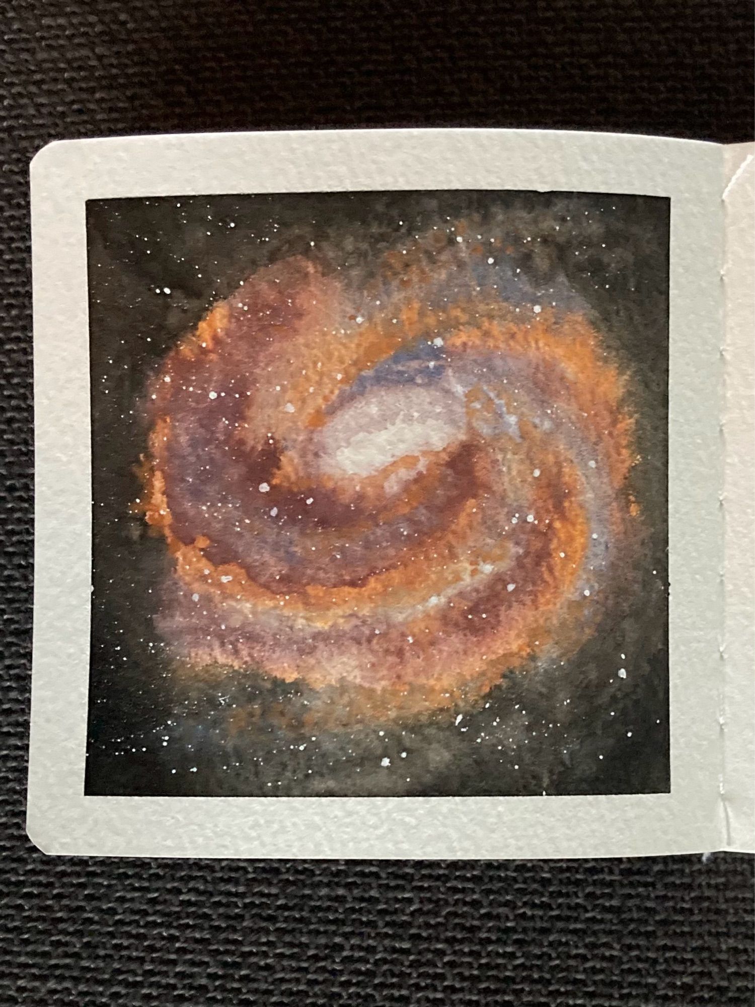 A watercolor painting of a donut-shaped spiral galaxy in space. The galaxy is comprised of swirling arms of burgundy, orange and bluish-grey circling a bright white centre. Stars are peppered throughout the galaxy and in the space surrounding it.