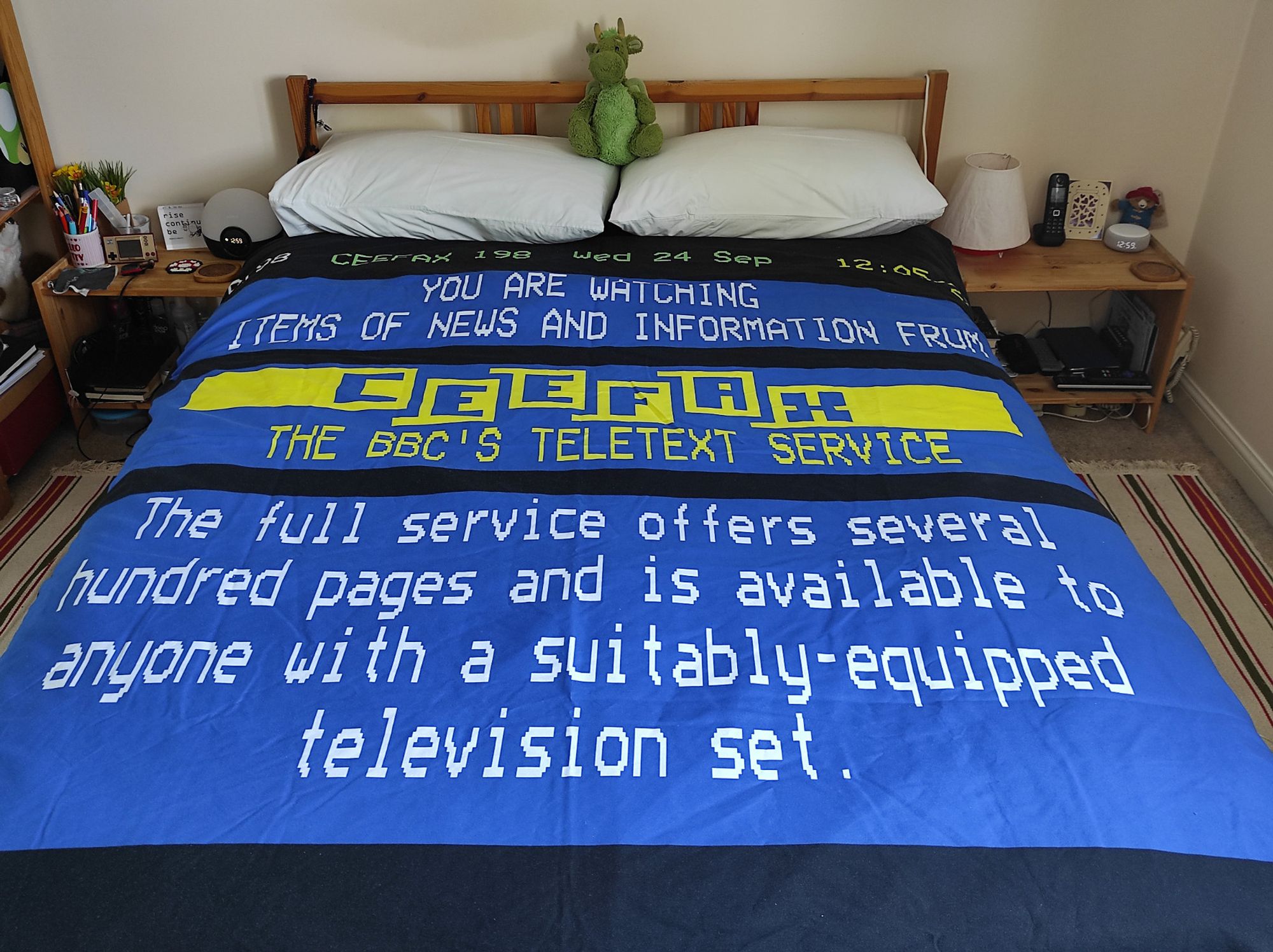 A picture of a bedroom with a double bed, on top of which is a duvet cover with a rendering of a Ceefax information page on it.