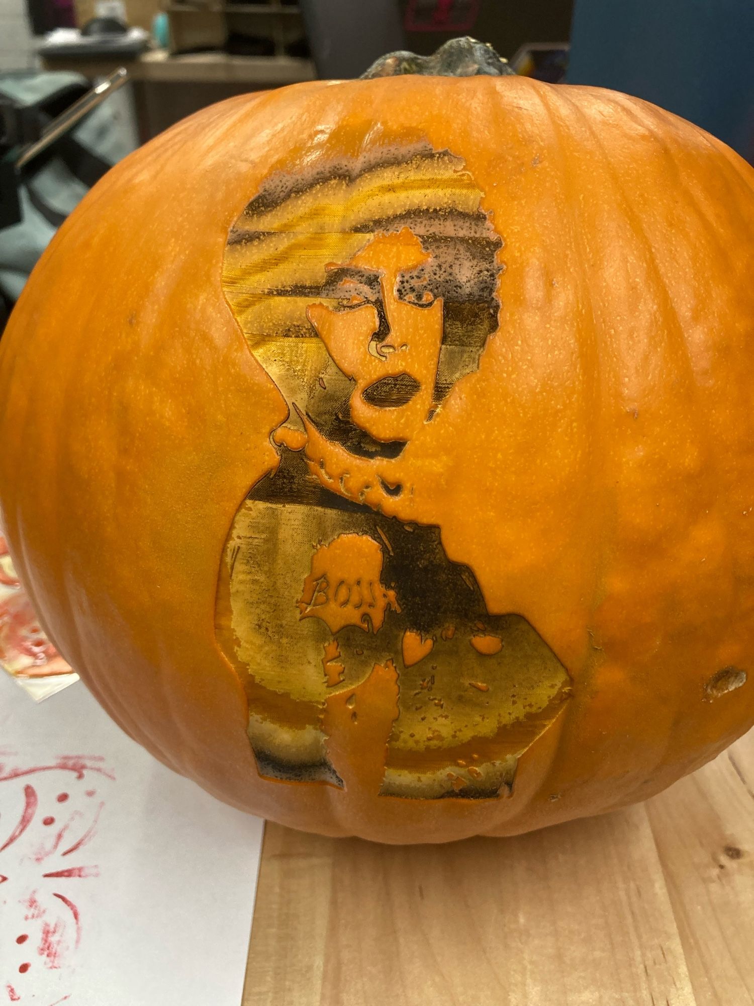 A medium orange pumpkin laser etched with a character from the Rocky horror picture show. The etching is uneven, and goes into different layers of the pumpkin, due to the pumpkin having to be rotated while etched