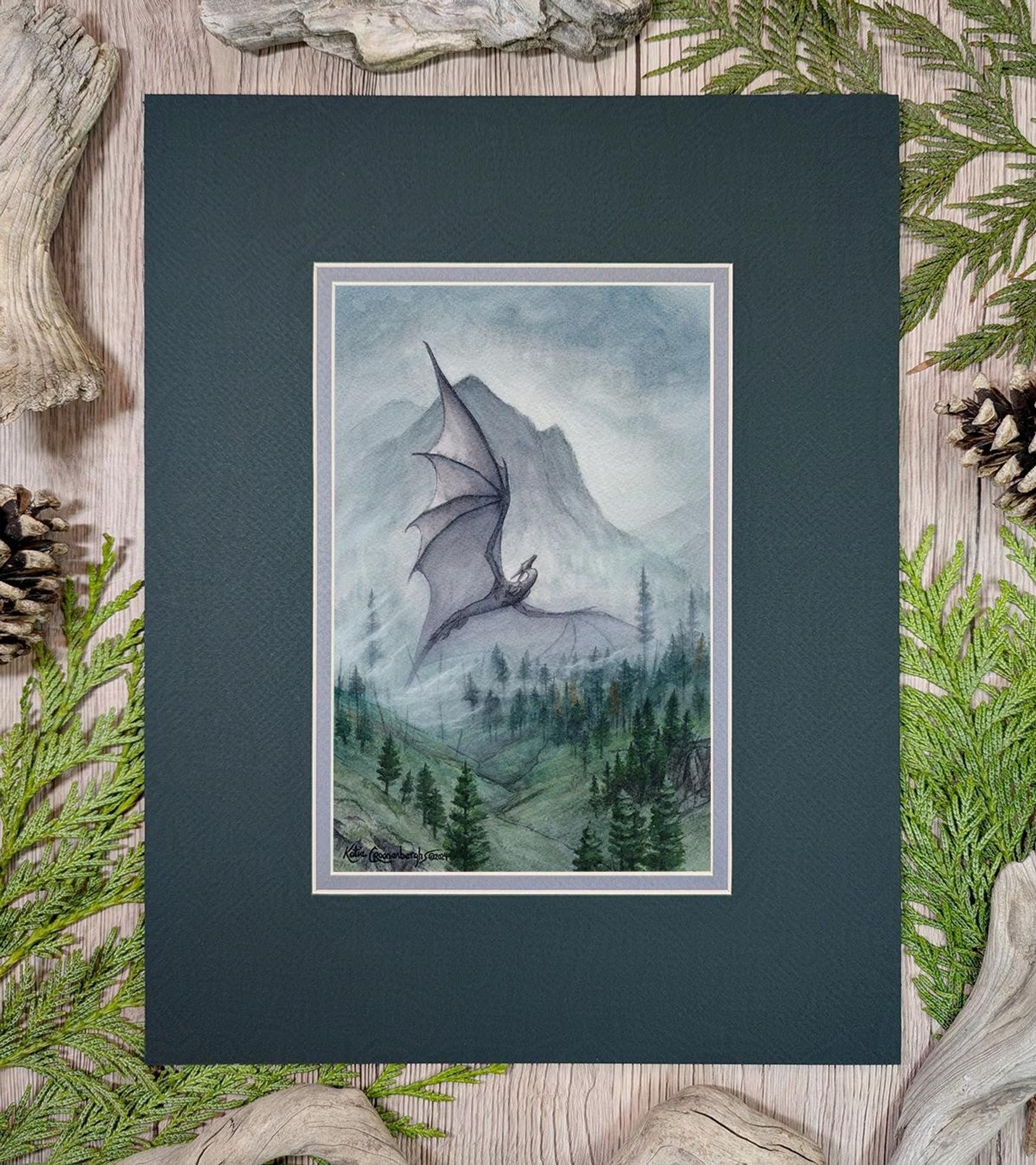 Watercolor and gouache painting of a dark gray dragon flying upward out of the mountain fog and mists. The shadow of a mountain rises in the distance and trees cover the green hillsides below. Painting is matted with a light gray inner mat and dark muted forest green top mat. 
Bottom left is artist signature Katie Croonenberghs 2024 and bottom right text is website kamakru.com