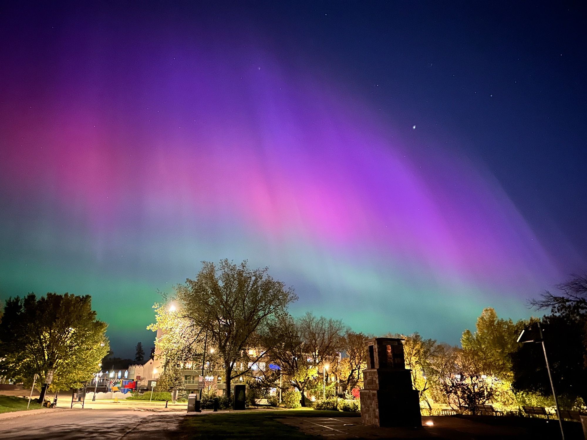 A photo showing a dark sky with a few stars, and massive bank of pink and green light