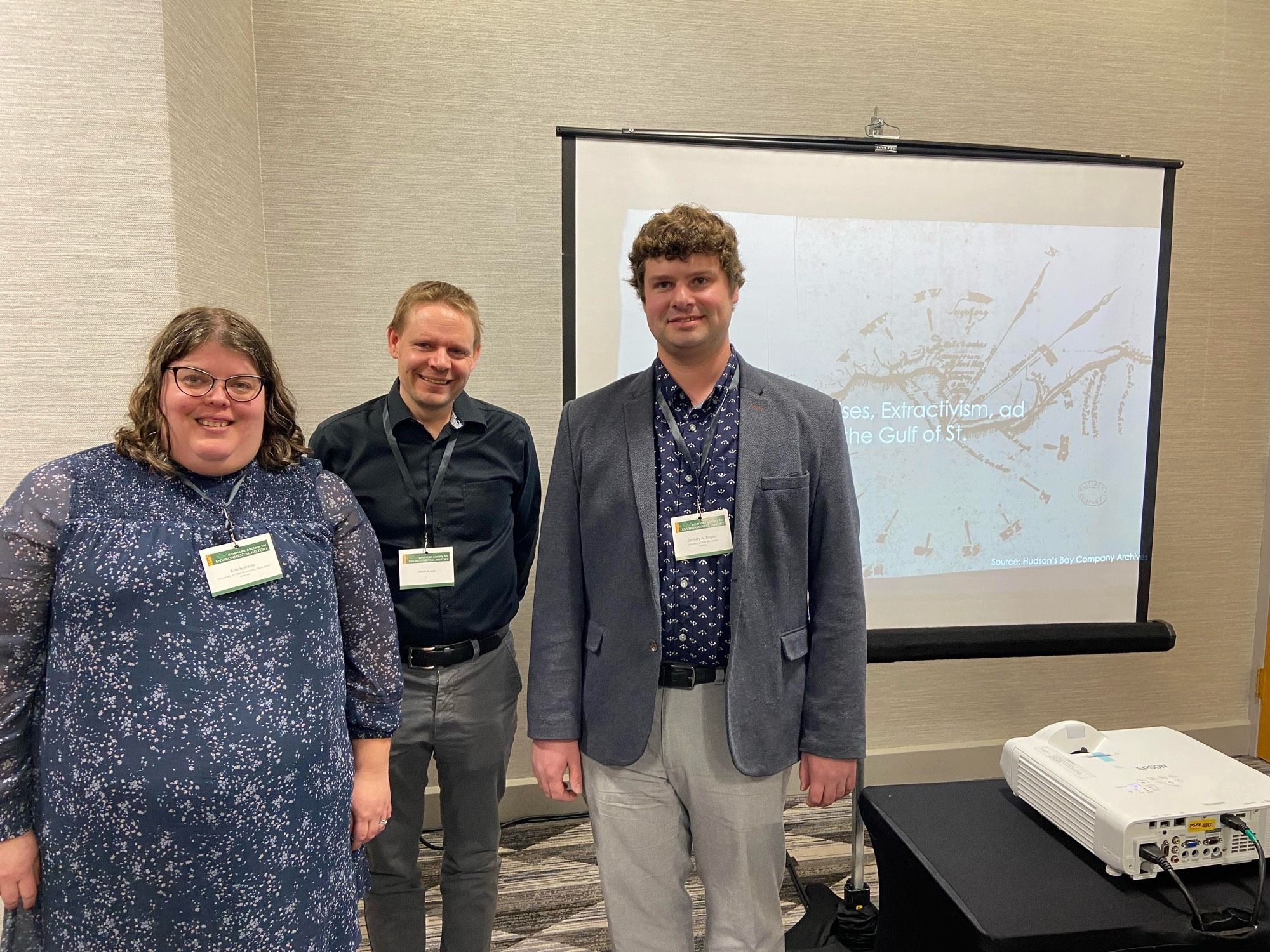 Three presenters standing in front of a conference slide.