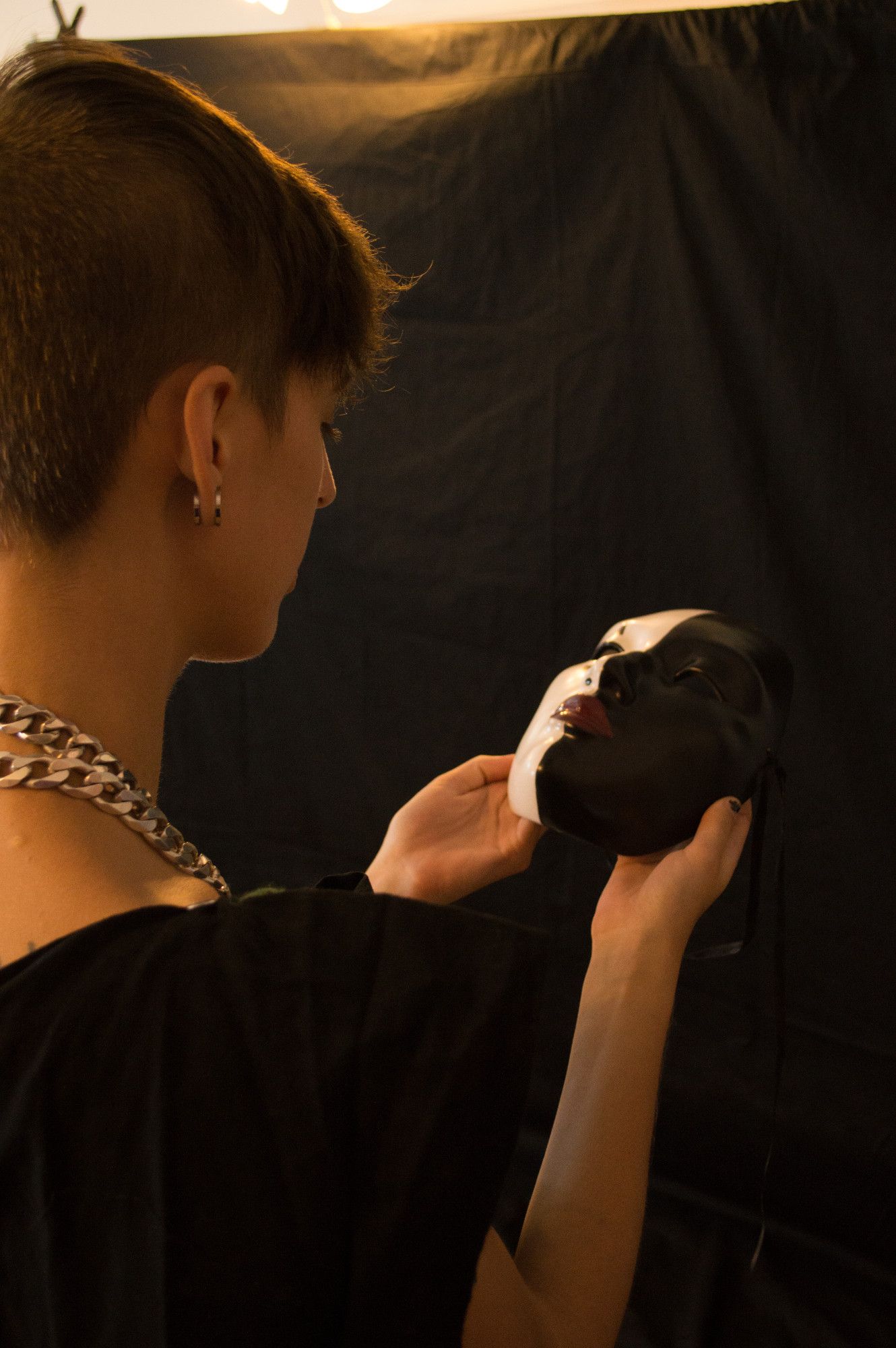 a skinny young white woman with short dark hair contemplates a black and white mask