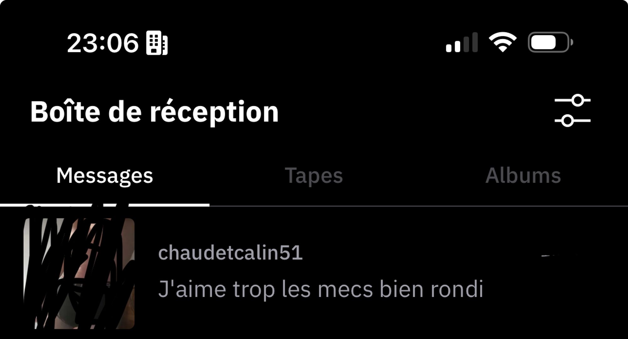 L'image montre une capture d'écran d'un téléphone portable. En haut de l'écran, on peut voir l'heure, 23:06, et les icônes de batterie, de signal mobile et de connexion Wi-Fi. En dessous, il y a un texte en blanc sur fond noir qui indique "Boîte de réception". Il y a trois onglets: "Messages", "Tapes" et "Albums", avec "Messages" sélectionné. En dessous, il y a un message d'un utilisateur nommé "chaudetcalin51". La photo de profil de cet utilisateur est partiellement masquée par des gribouillages noirs. Le message affiché est:

"J'aime trop les mecs bien rondi"