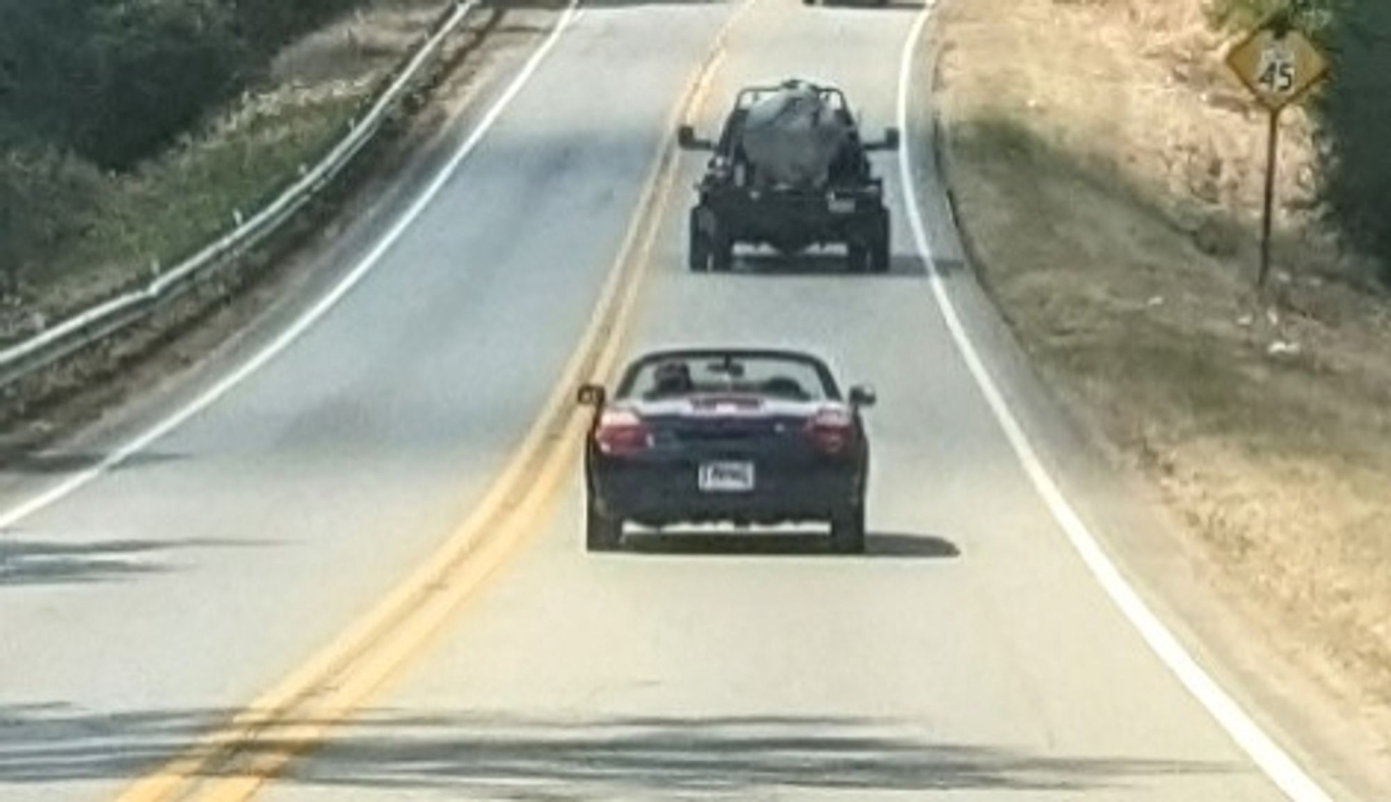 Black convertible car on the highway following a septic tank truck (not seen: horrible stinky odor)