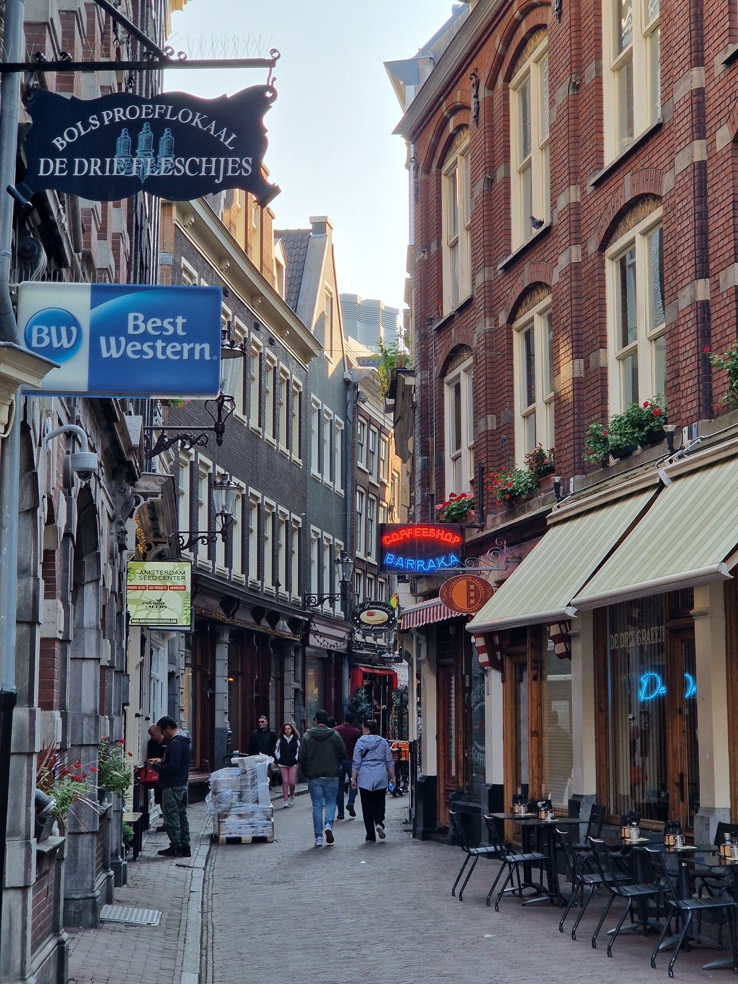 A small street with 2 story buildings either side, some chairs and tables ok the street and signs for several stores on either side