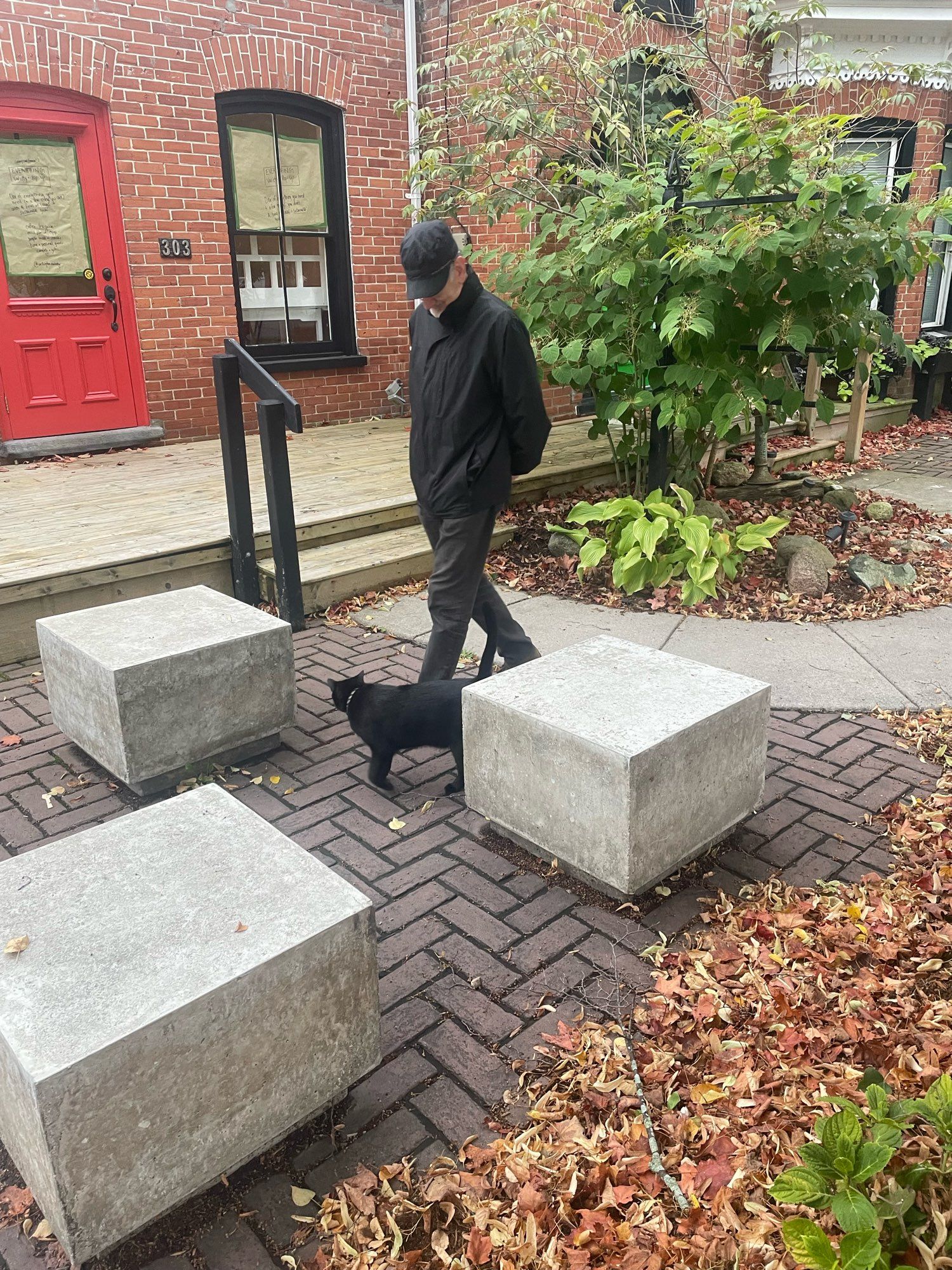 A black cat at the feet of a man (also in all black) as they make their way through three concrete cube benches