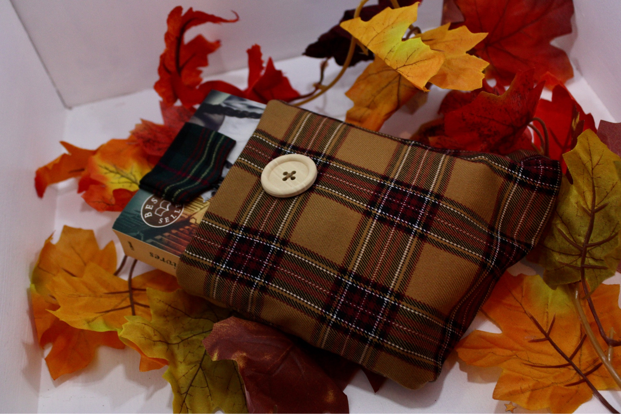 Pochette cousue dans un tissu tartan jaune et rouge. Un livre dépasse de la pochette, avec un marque pages réalisé dans un tissu tartan dans les tons vert sapin et rouge