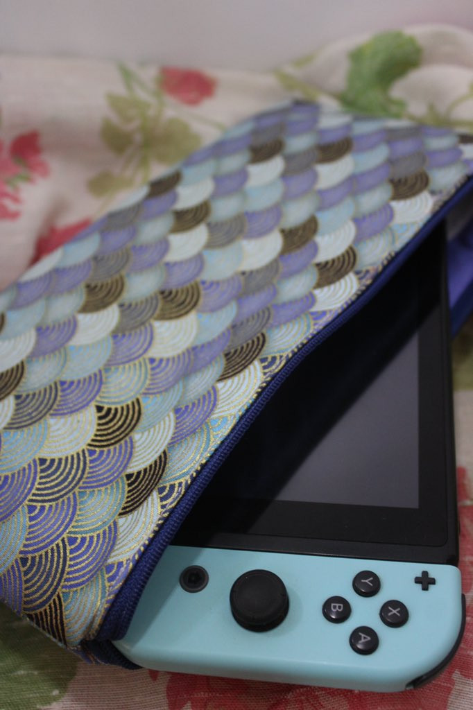 Photo d'une pochette à Switch bleus à vagues. La pochette se referme avec une fermeture éclair bleu foncé. On peut voir une console de jeux à moitié sortie de la pochette