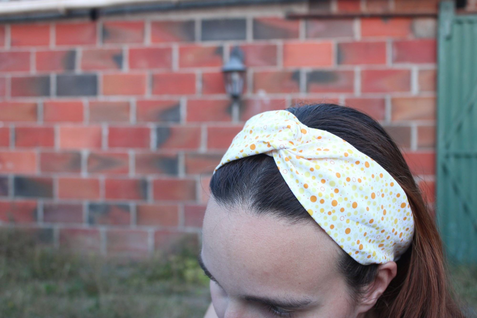 Gros plan sur un headband porté, réalisé dans un tissu blanc à pois jaune et orange