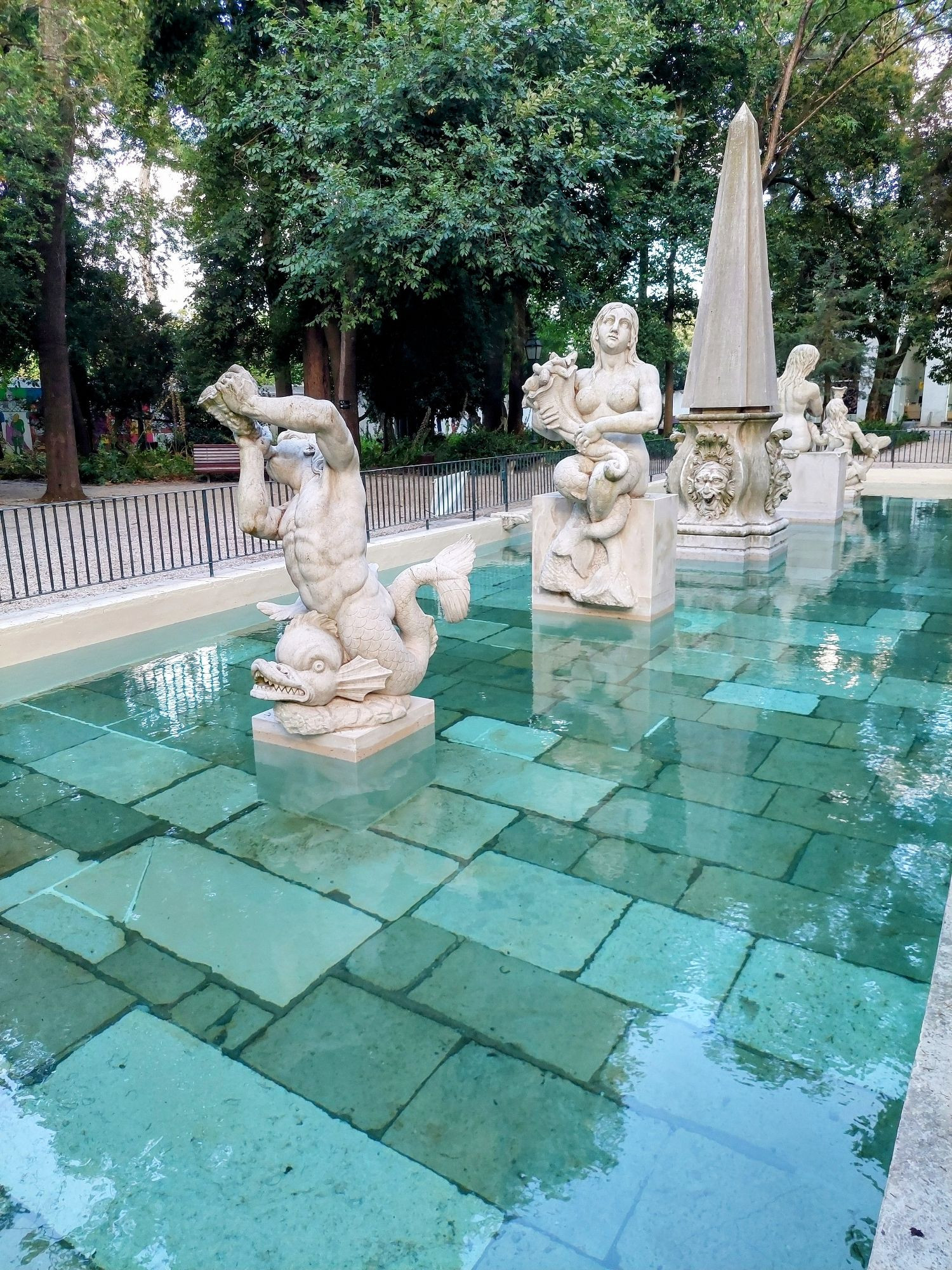 Mehrere steinerne Statuen stehen in einem Wasserbecken, die Farbe des Wassers ist grün