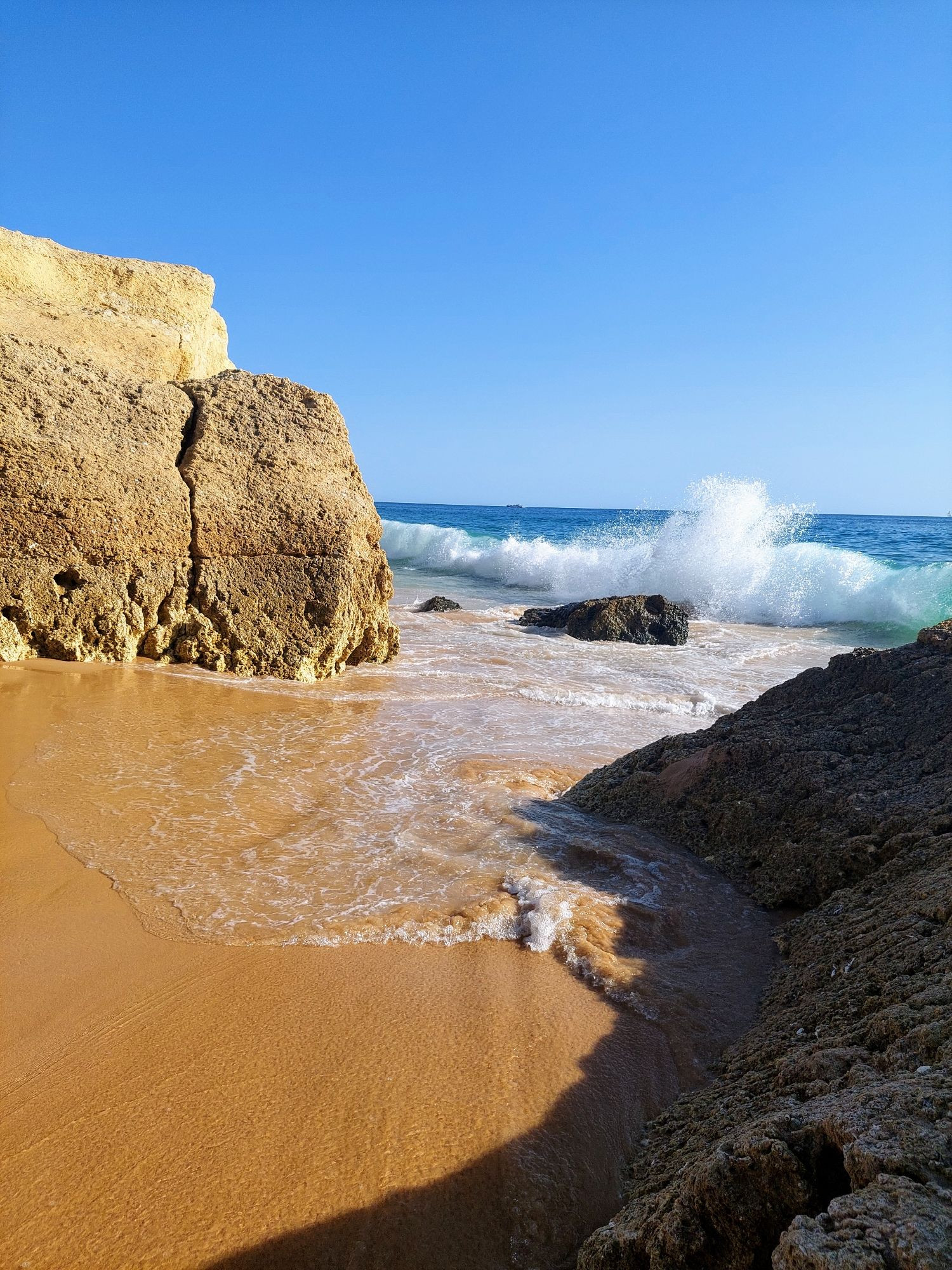 Strand mit Felsen, im Hintergrund das Meer und blauer Himmel