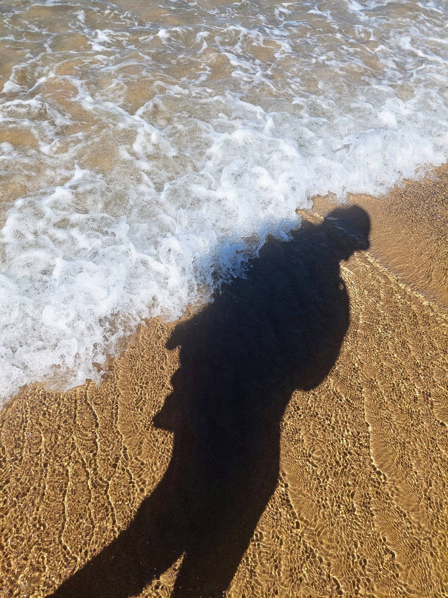 Am Strand, Wellen treffen auf den Schatten einer Person