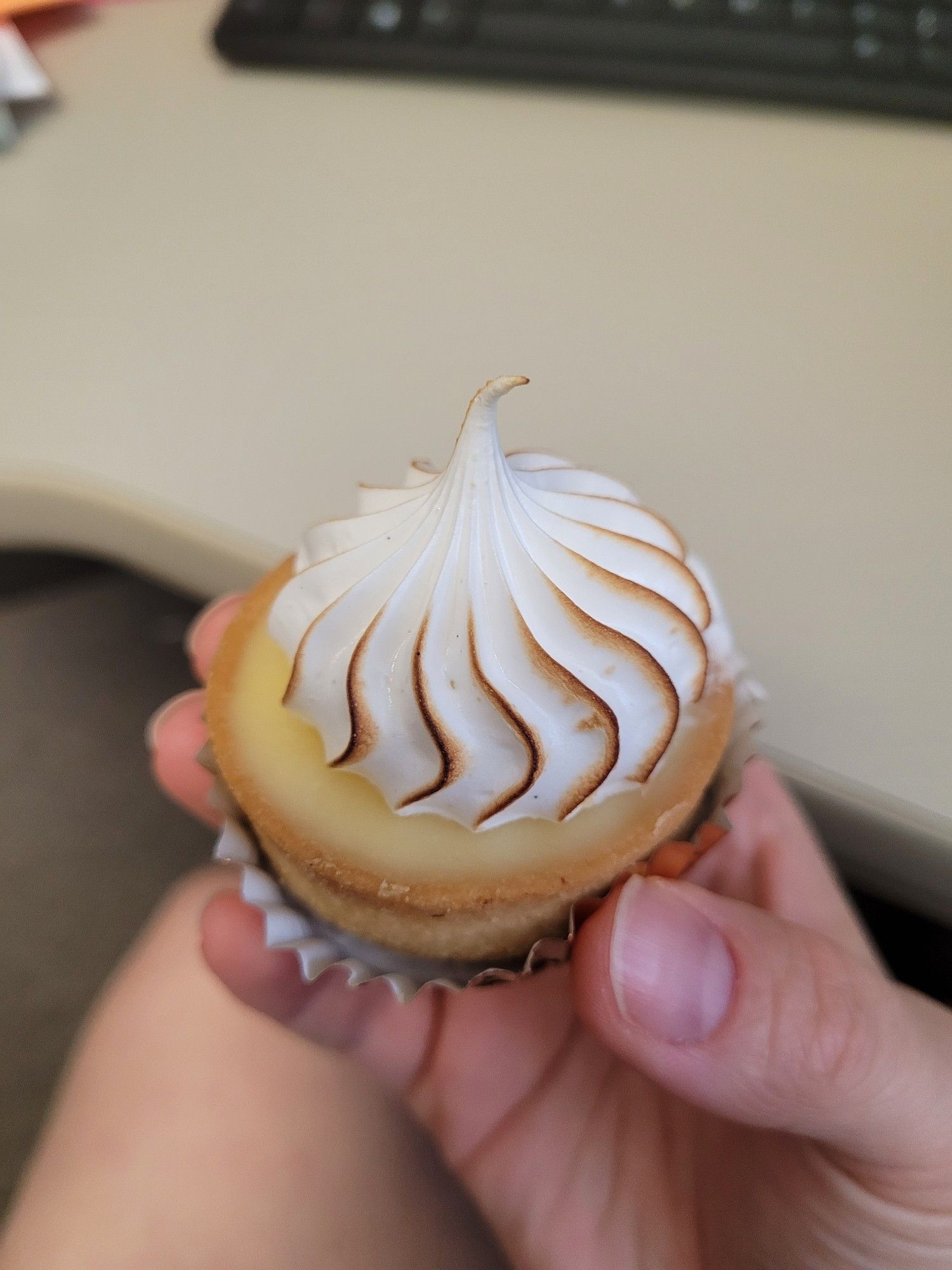 A hand holding a tiny lemon tart with Swiss meringue