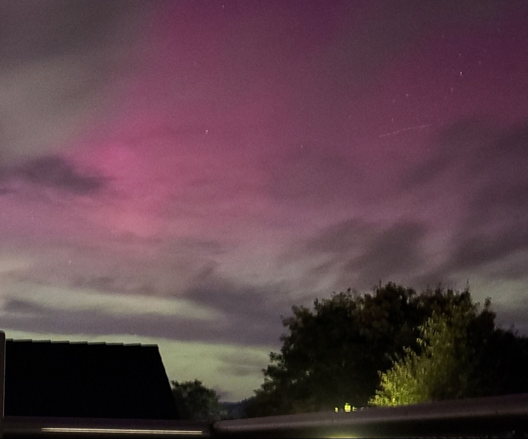 Polarlichter am Himmel, am unteren Bildrand das Geländer des Balkons. Links im Bild das Dach einer Garage, rechts Bäume.