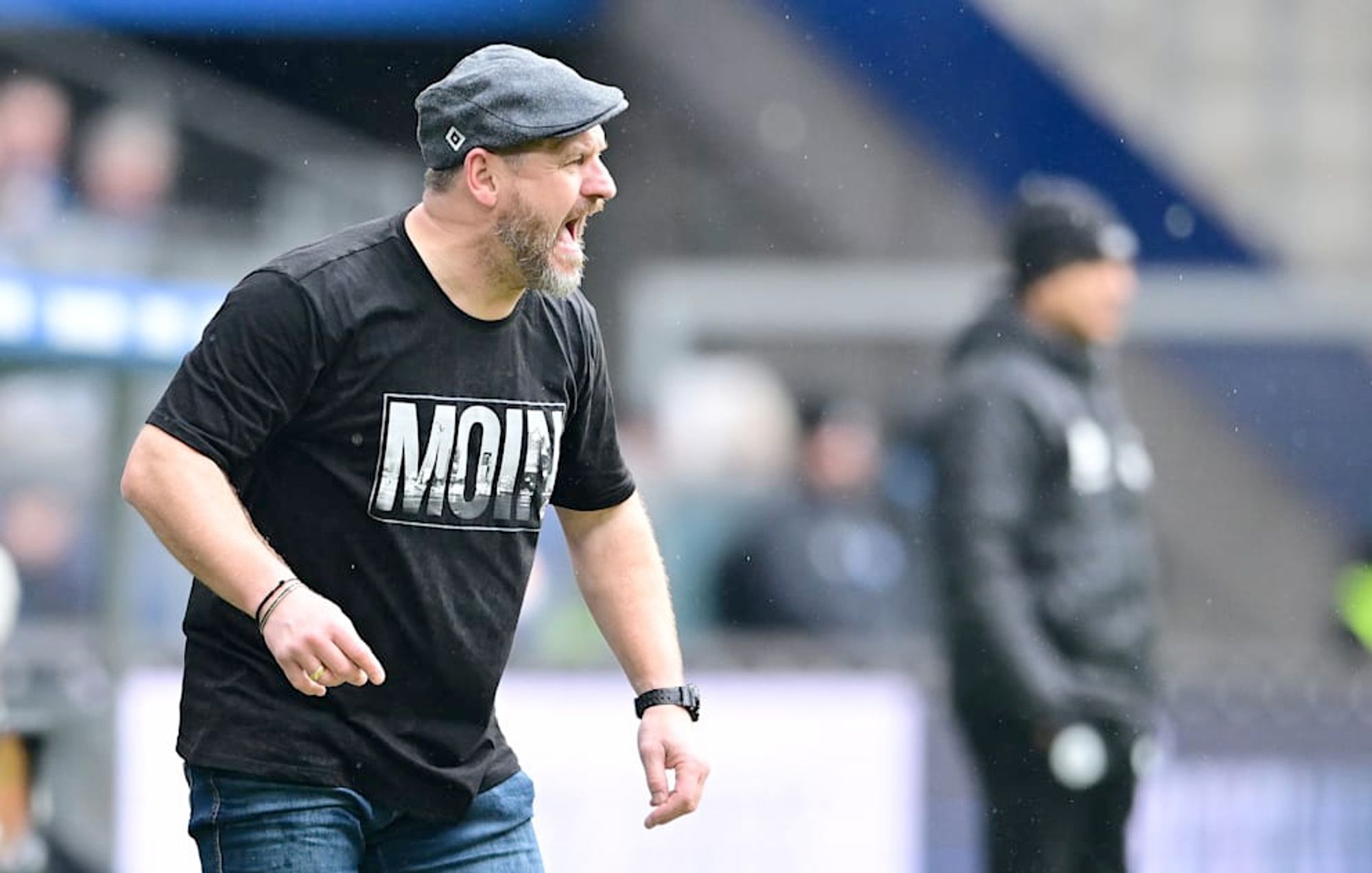 Steffen Baumgart in his trademark flat cap and casual touchline attire.