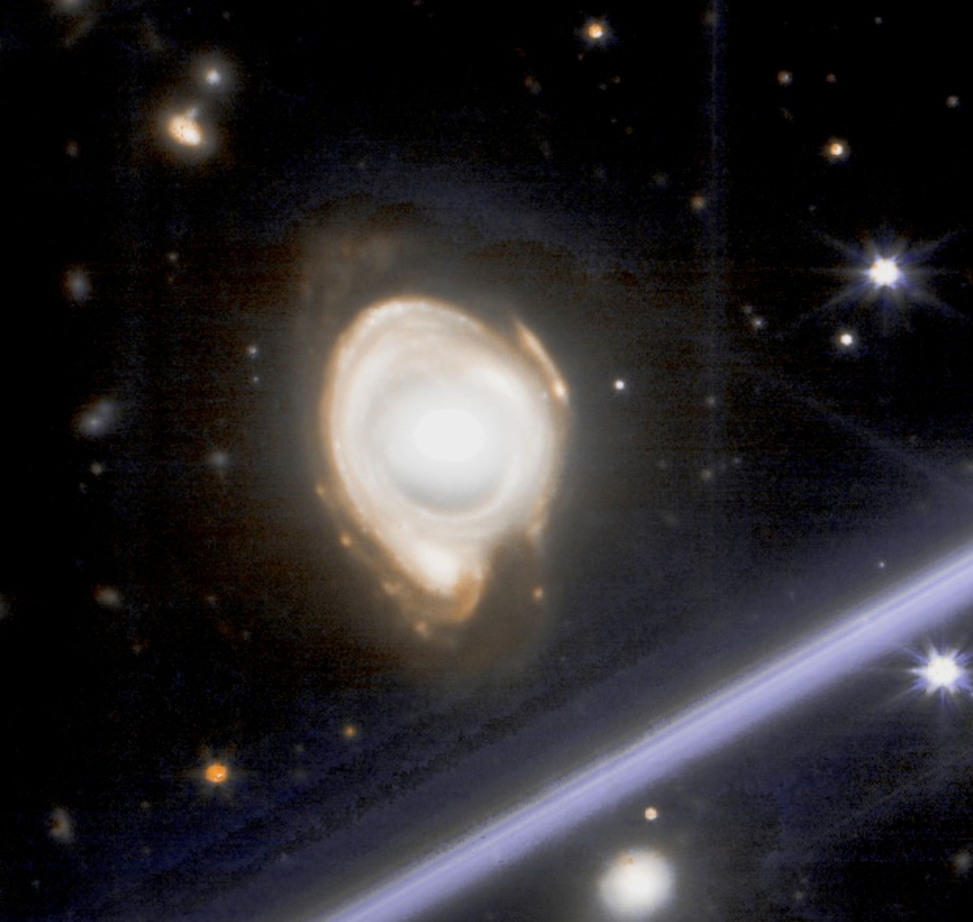 A NIRCam image of a lensed galaxy, showing a distorted, ring-shaped galaxy with a bright center and a faint outer halo. The galaxy appears to be magnified and stretched due to gravitational lensing by a massive object in the foreground.