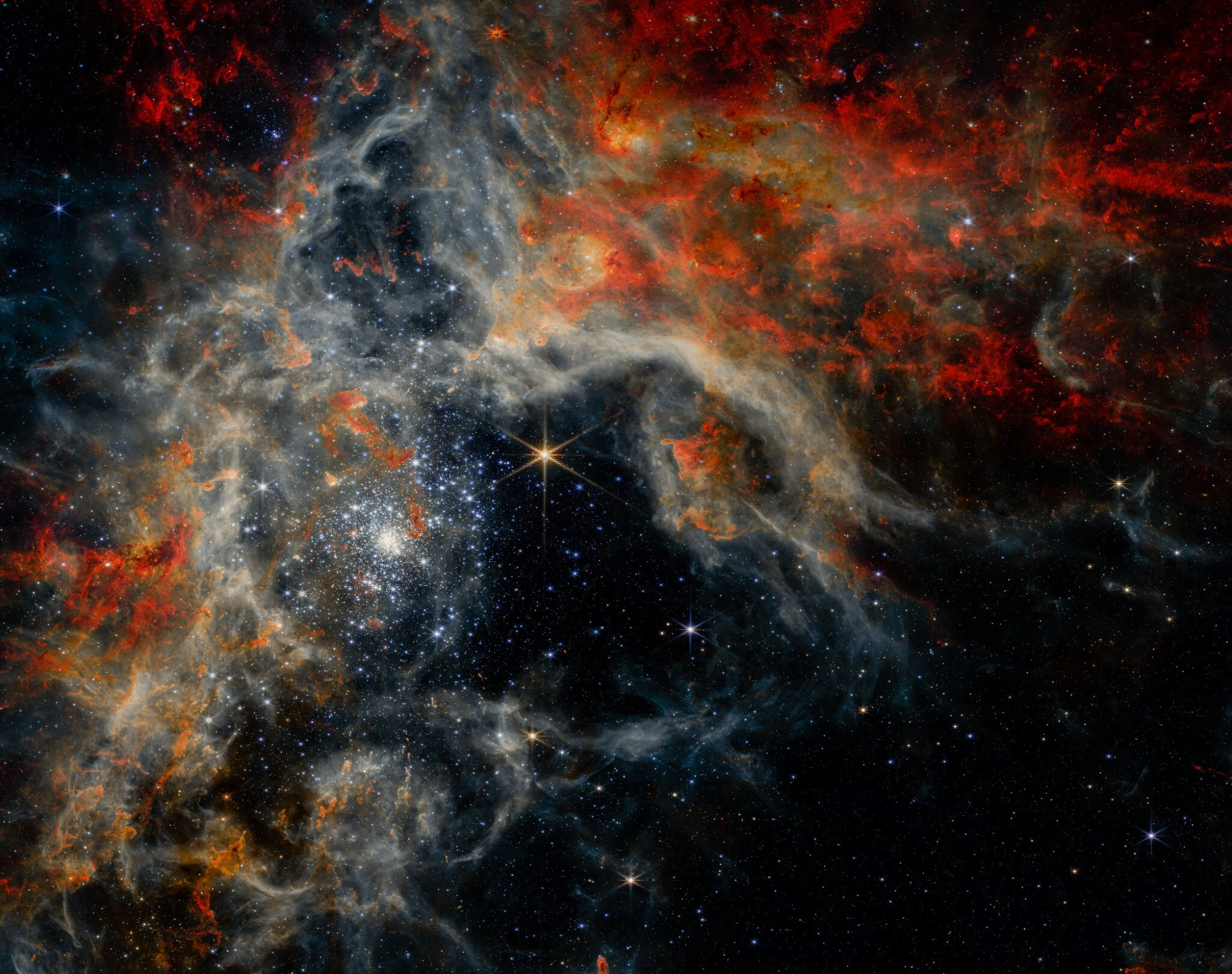 A vibrant, high-resolution image of the Tarantula Nebula (30 Doradus) captured by the James Webb Space Telescope's Near-Infrared Camera (NIRCam). The image showcases a cosmic landscape filled with swirling clouds of gas and dust, illuminated by countless stars in various stages of formation. The colors, ranging from deep red to vibrant blue, depict the different elements and temperatures within the nebula.