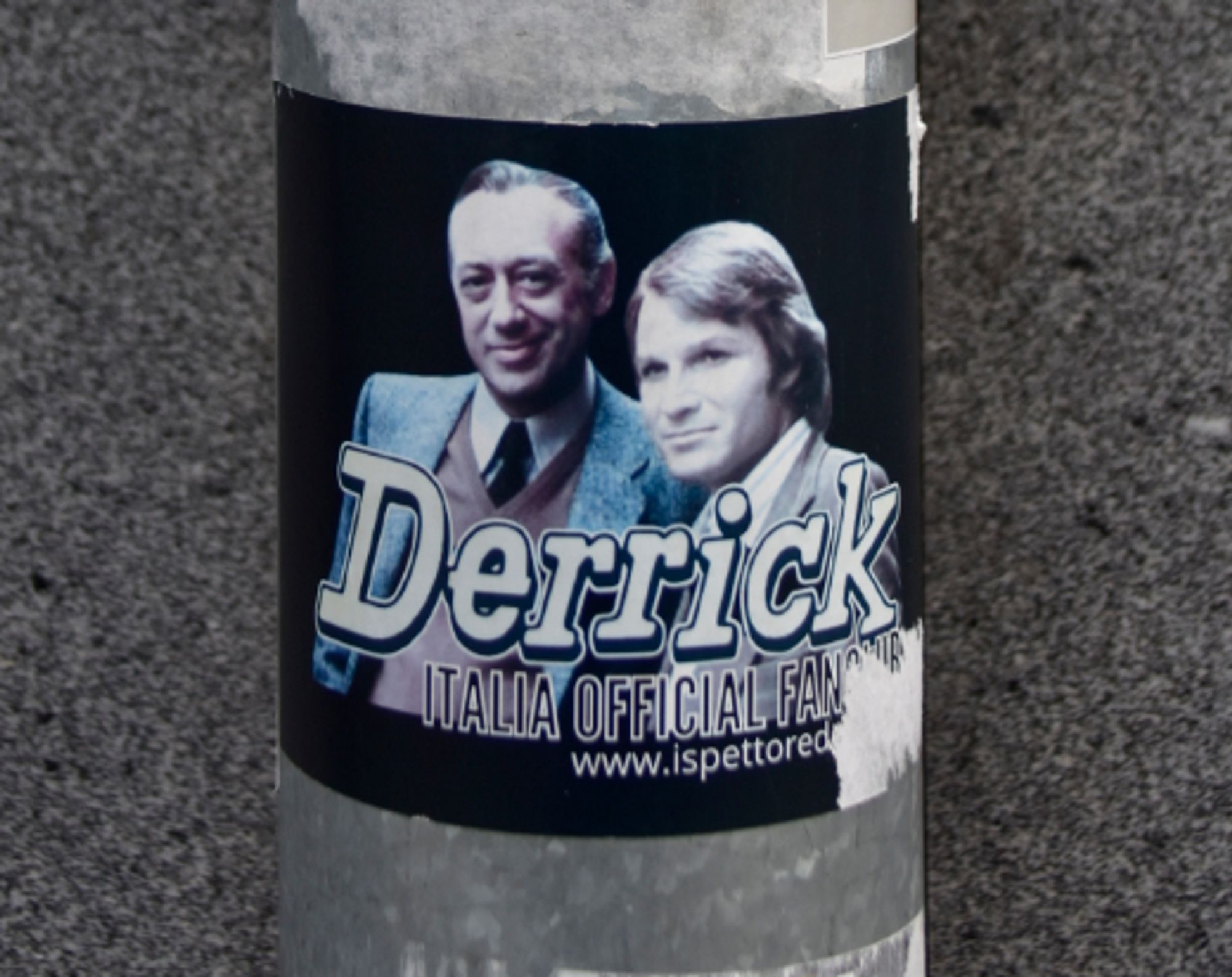 Photo d'un sticker collé sur un tuyau d'évacuation d'eau d'u  immeuble. Dessus il y a la photo de Derrick et de son acolyte et c'est ecrit Derrick Italia Official Fanclub avec une adresse www.ispettored.it (je suis pas sûre de la fin le stickes était un peu abîmé)