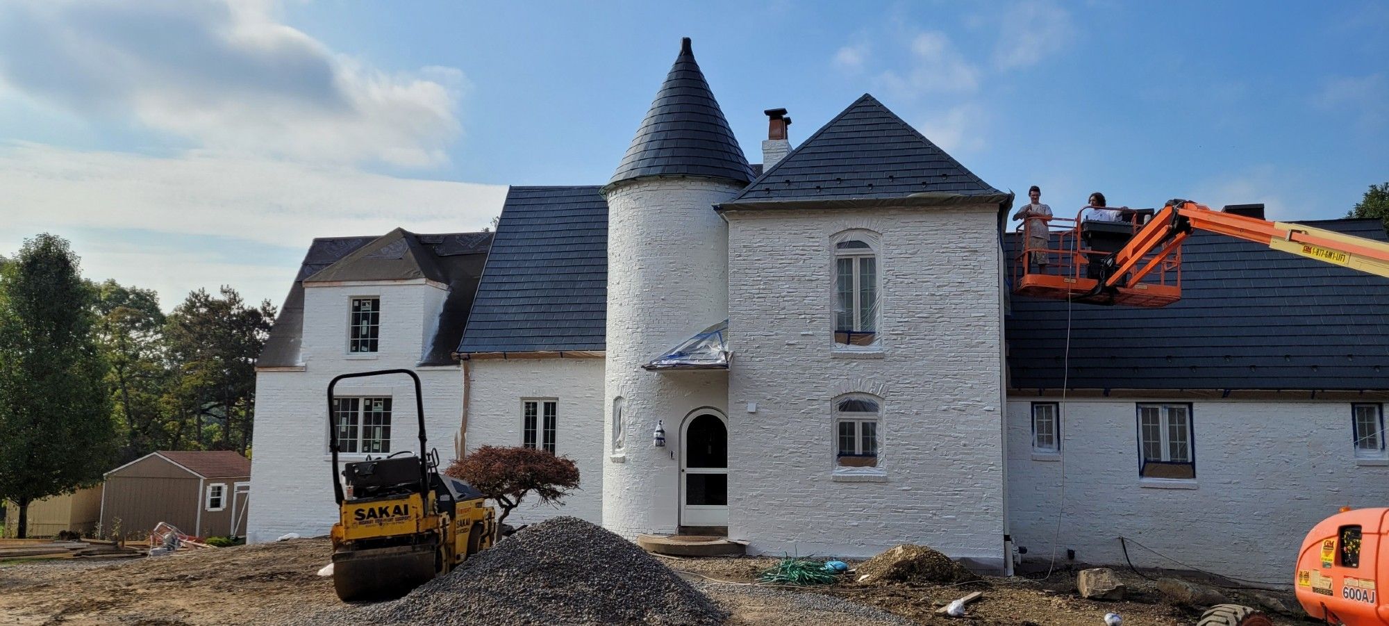 Estate sized home with white painted masonry, a central turret, and a metal rool made to look like blue slates