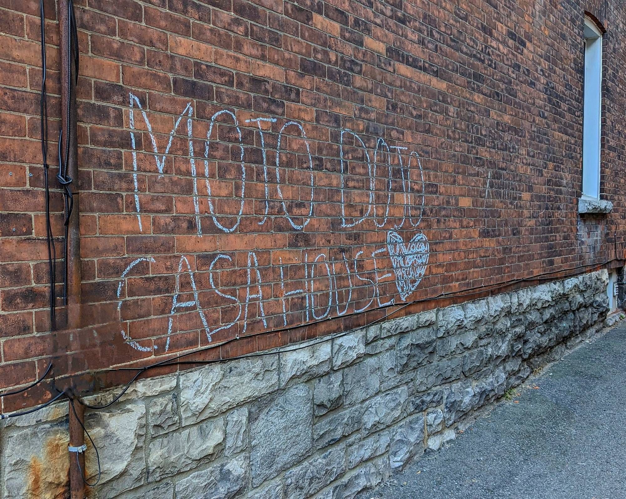 Brick wall on the side of a house with the words "mojo dojo casa house" written in chalk