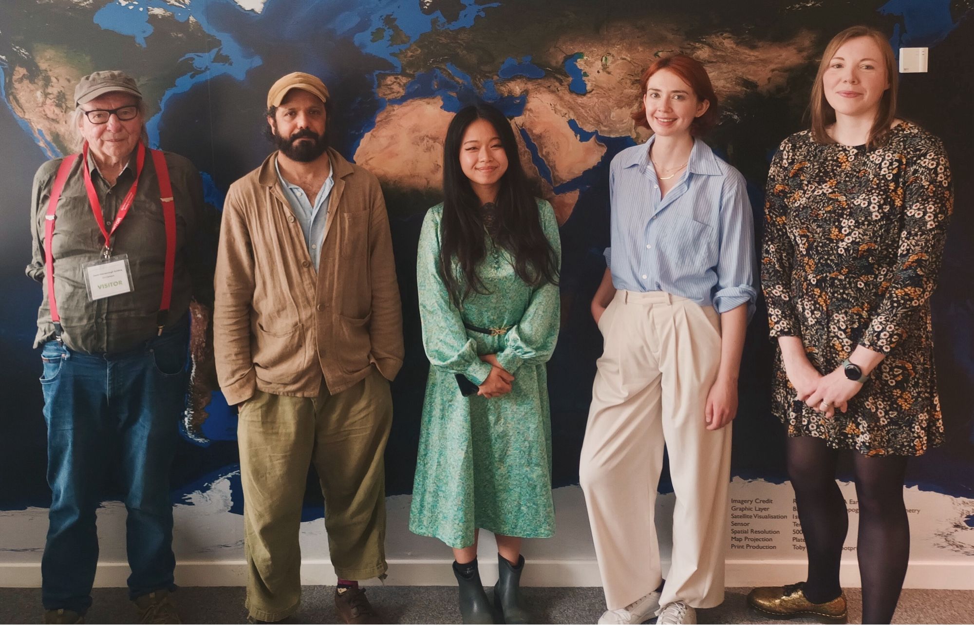 A row of people standing in front of a map of the world at CCI, two if them are wearing hats, three of them are not. The next post will explain who they are in a tick.