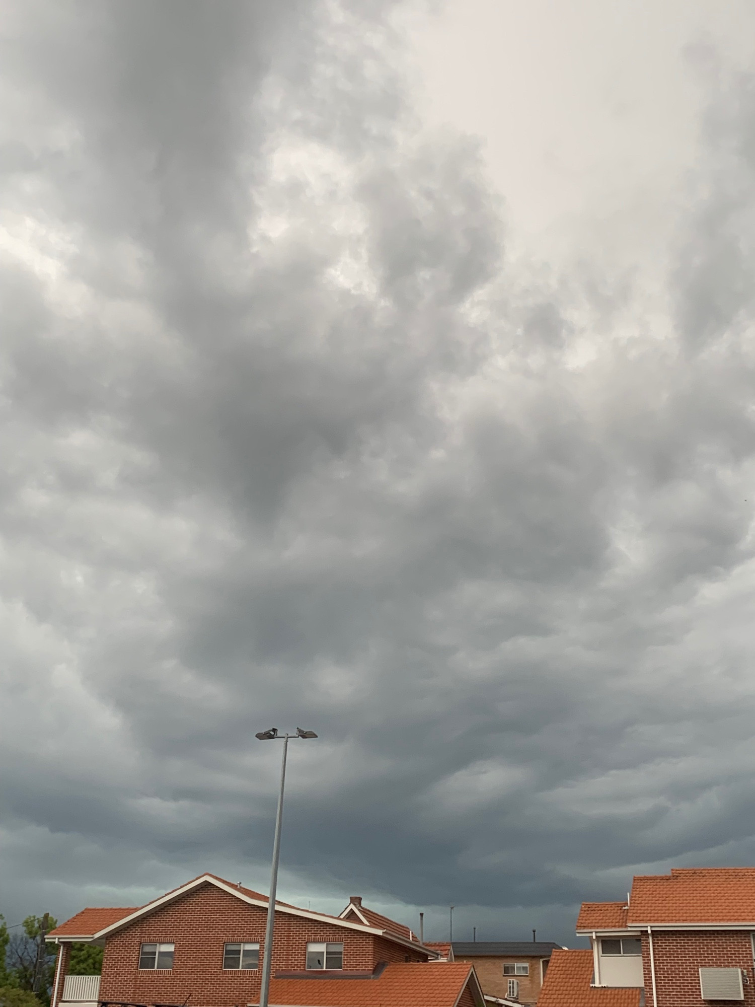 Heavy, malignant, grey clouds hovering over terracotta coloured houses.