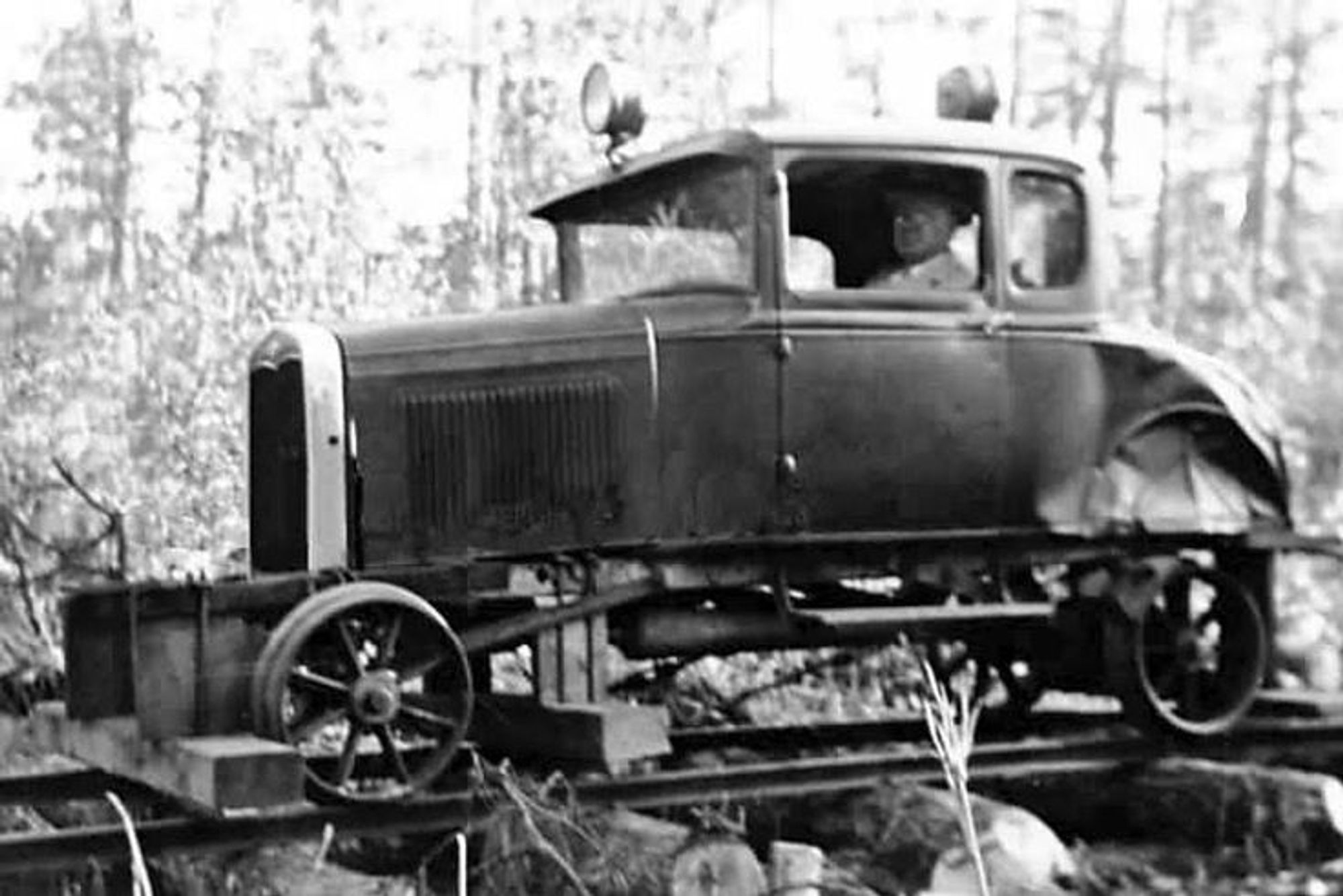 A Ford coupe modified to run on rails using cast steel wheels. A crude pilot made of lumber is strapped to the front of the car, and a pair of electric headlights mounted to the roof fore and aft.