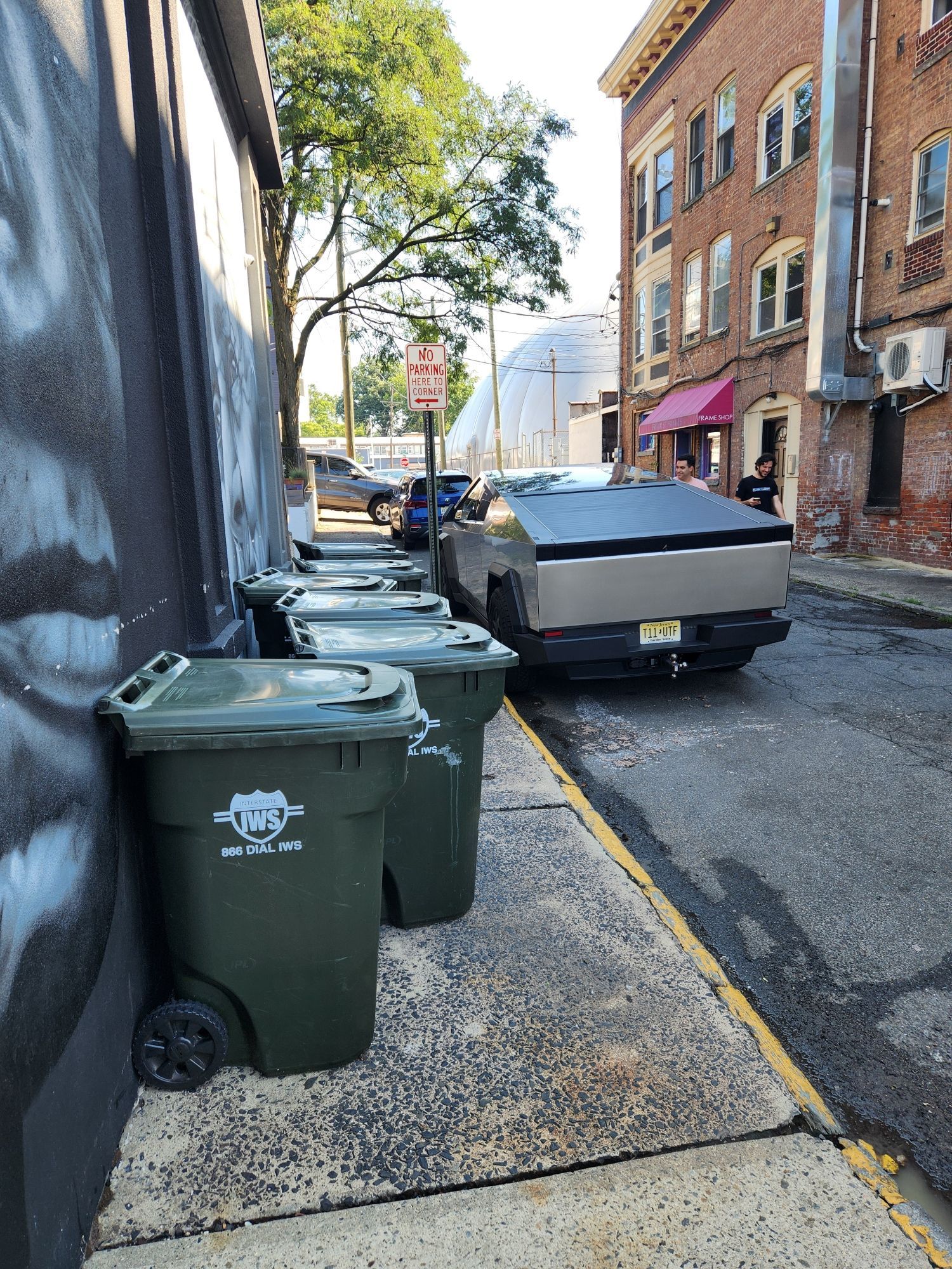 A cyber truck parked next to a line of wheelie bins